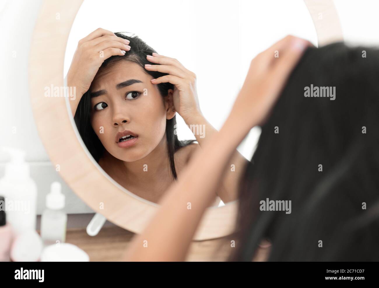 Worried asian woman checking her hair in mirror at home Stock Photo
