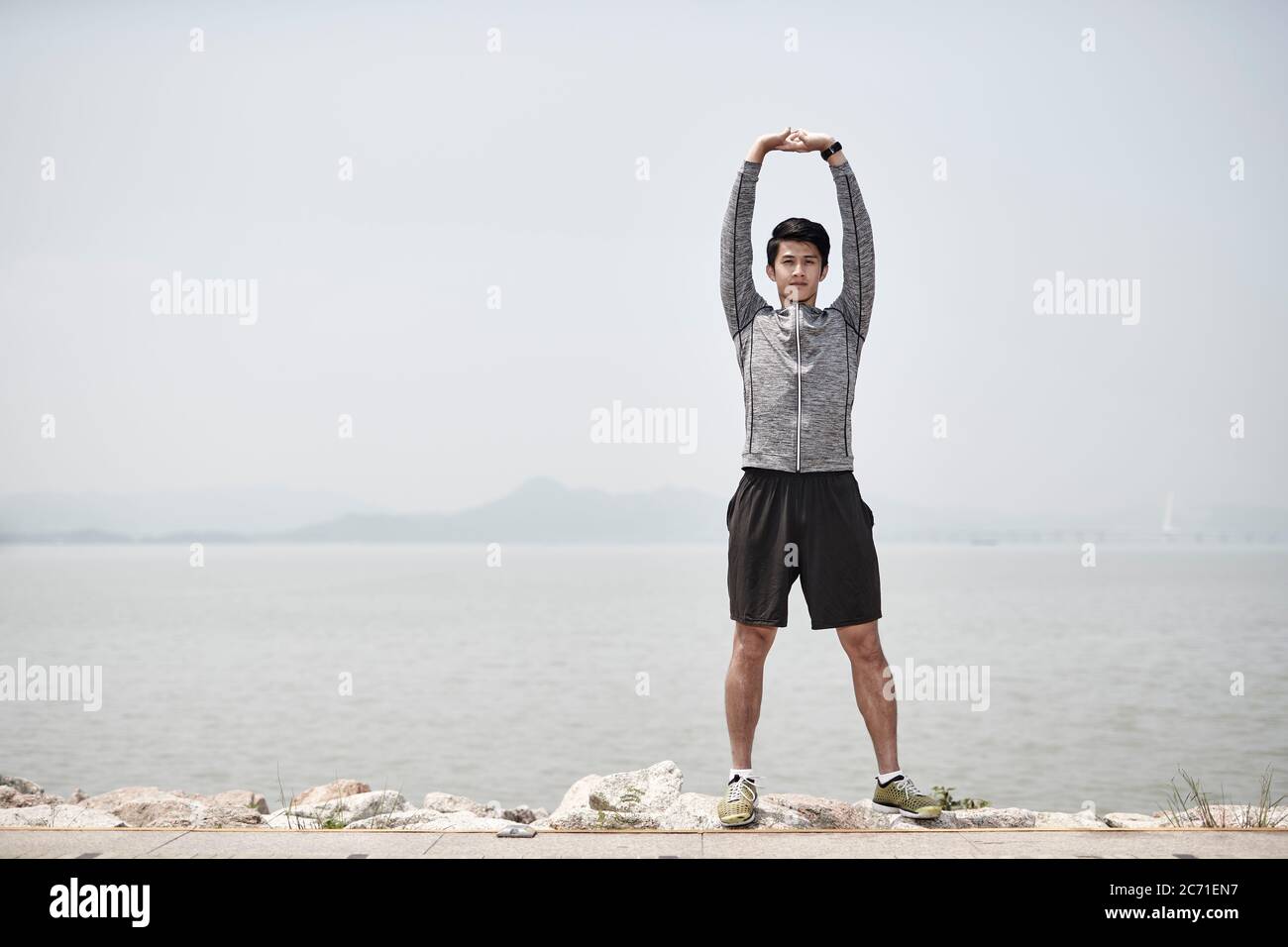 young asian adult man stretching arms outdoors by the sea Stock Photo