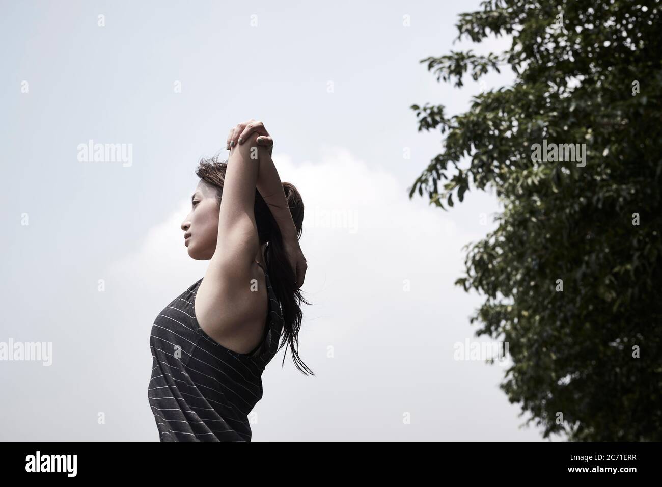 young asian adult woman stretching arms outdoors, low angle side view Stock Photo