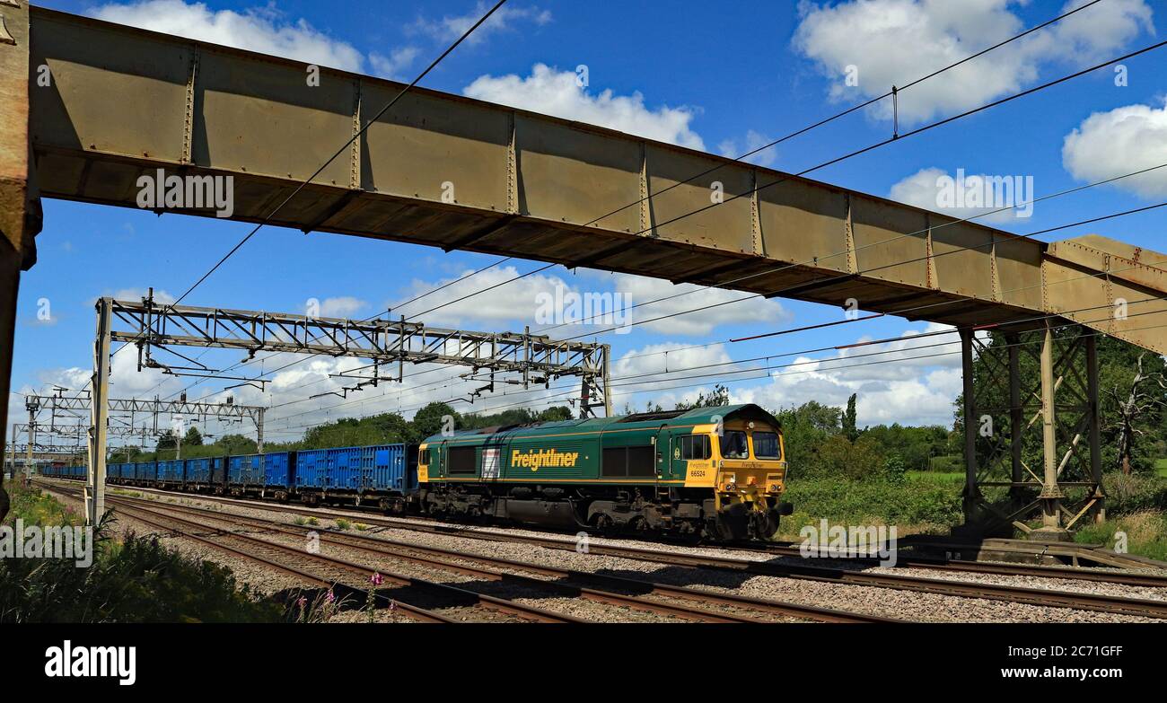Freightliner diesel locomotive no 66524 passes under a foot bridge to the south of Acton Bridge station on train of empty refuse from Runcorn. Stock Photo