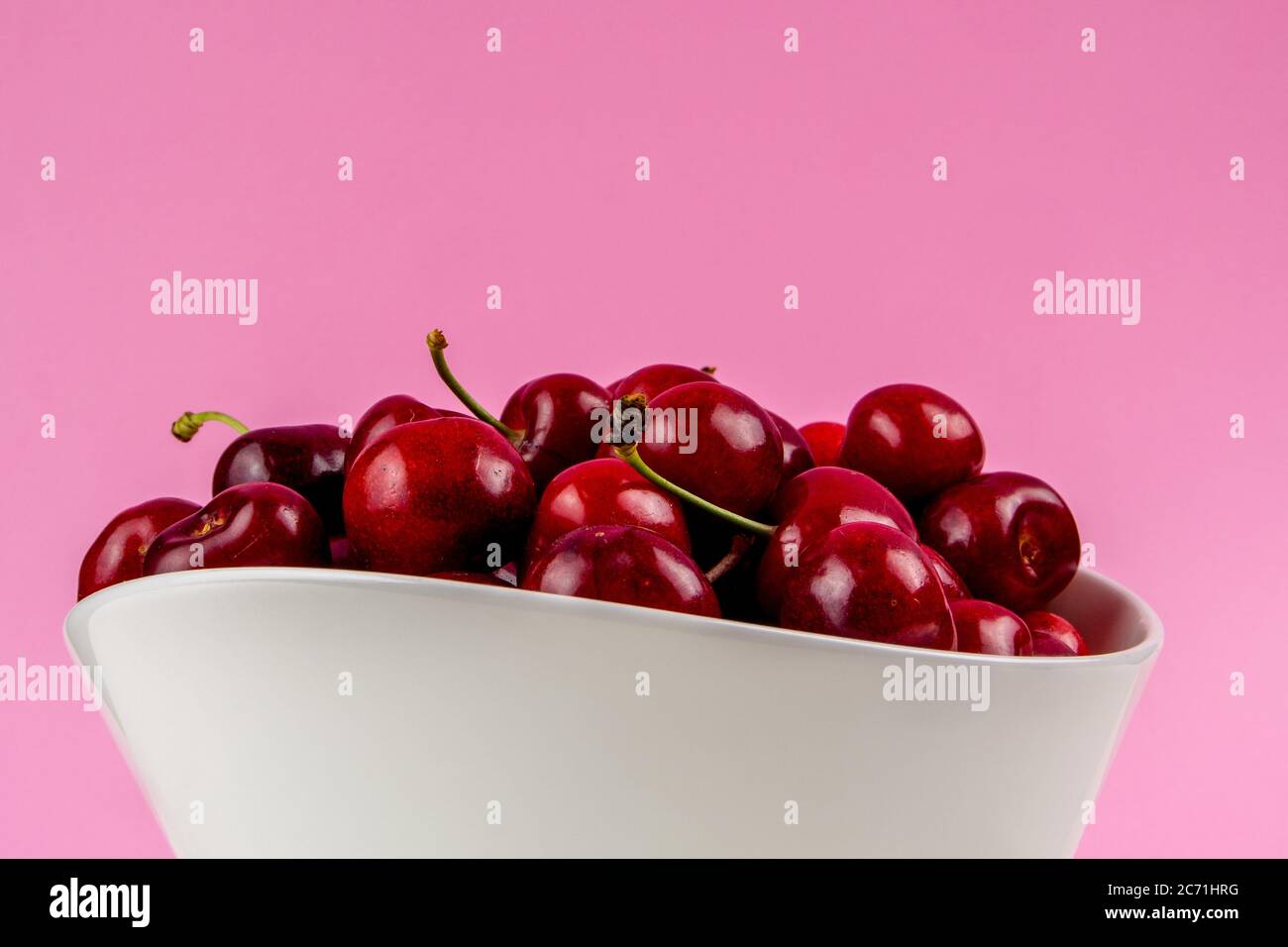 collection of many cherries in white ceramic bowls on pink background