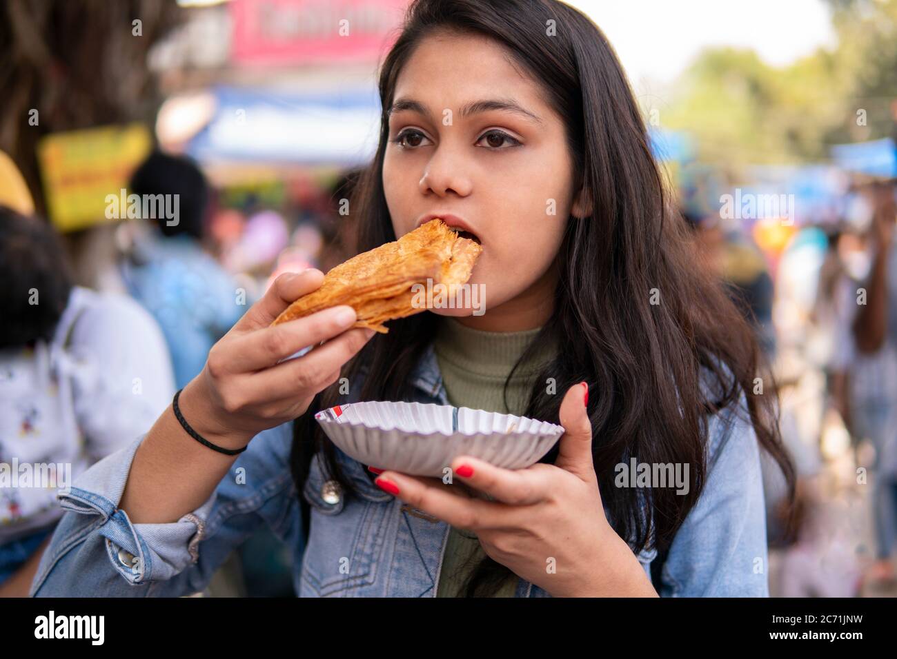 Girl eating street food potato puff pastry (Aloo patties) at outdoor street market at day time. Shoot location Sarojini Nagar, Delhi, India. Stock Photo