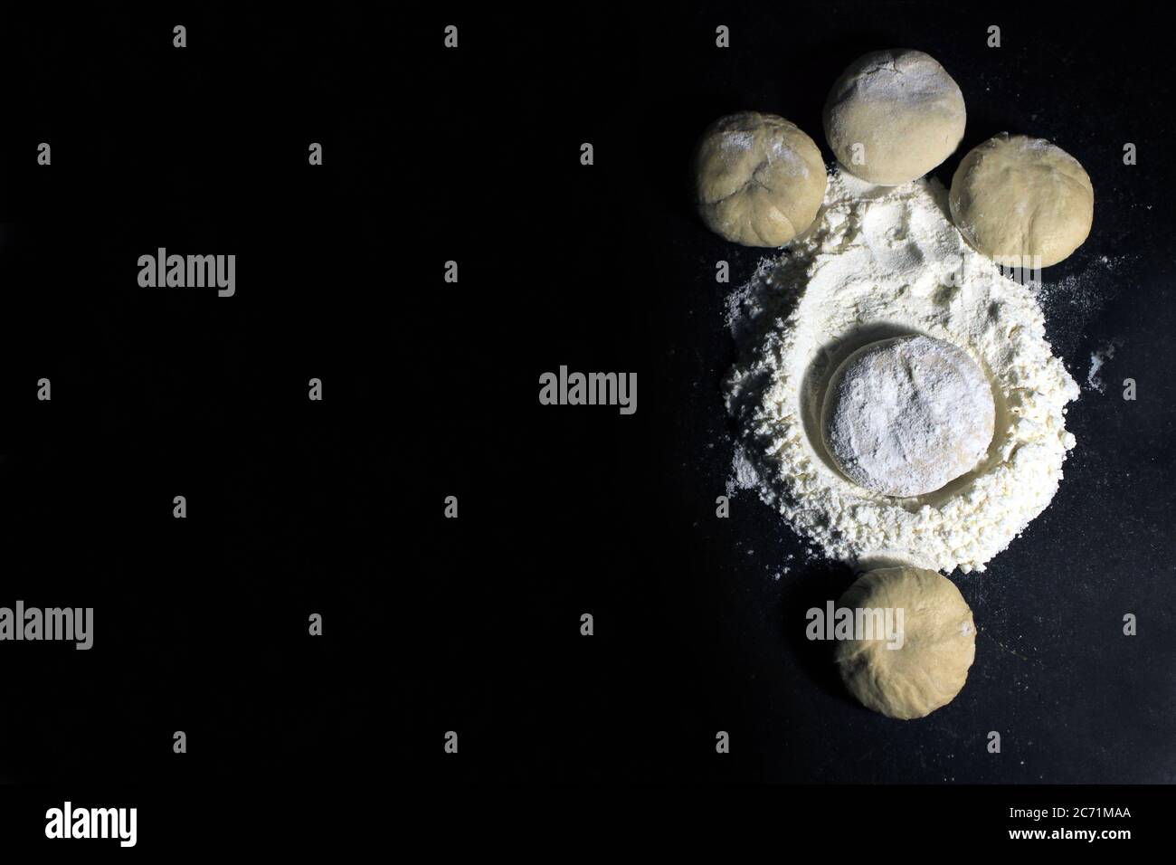 Piece of yeast dough with wheat flour on black background. Unbaked