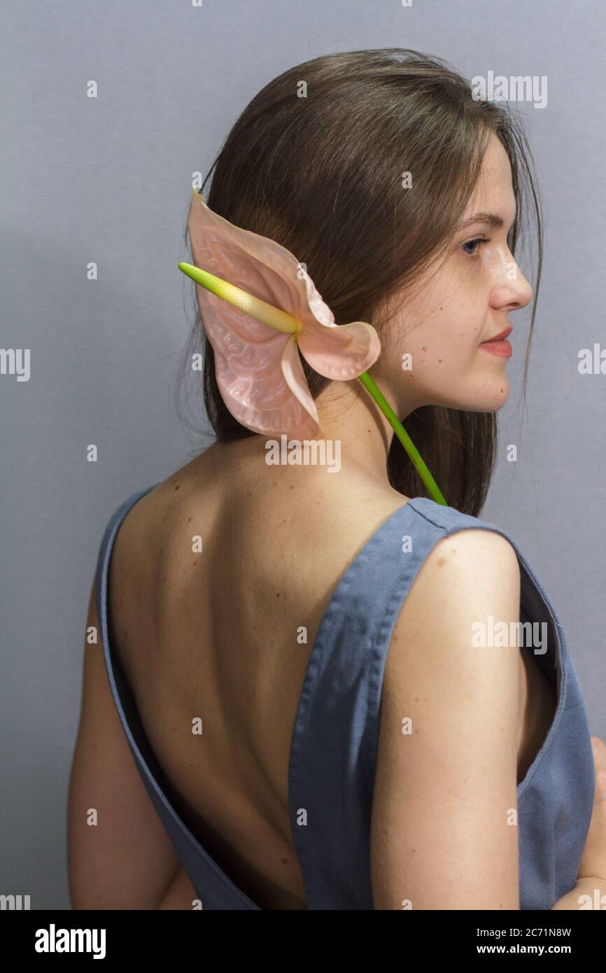 Sensual portrait of long-haired brunette girl with pink Anthurium flower on gray background Stock Photo