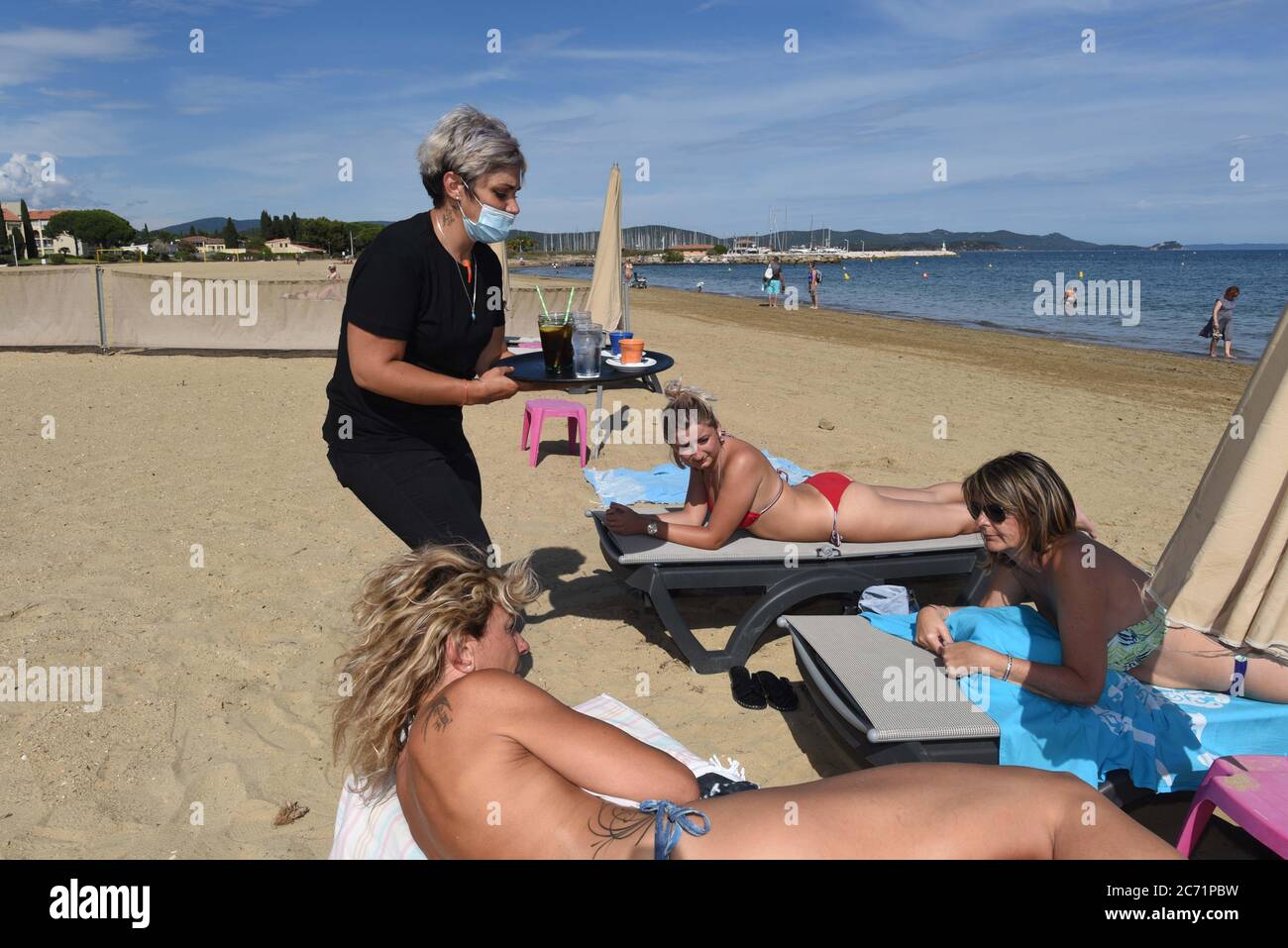 *** STRICTLY NO SALES TO FRENCH MEDIA OR PUBLISHERS - RIGHTS RESERVED ***June 07, 2020 - La-Londe-les-Maures, France: Cynthia, a waitress at La Voile Plage, brings drinks to customers sitting on deckchairs on the beach. She has to wear a facemask against covid-19. Most beaches have been reopened as French authorities gradually ease the coronavirus lockdown. Stock Photo