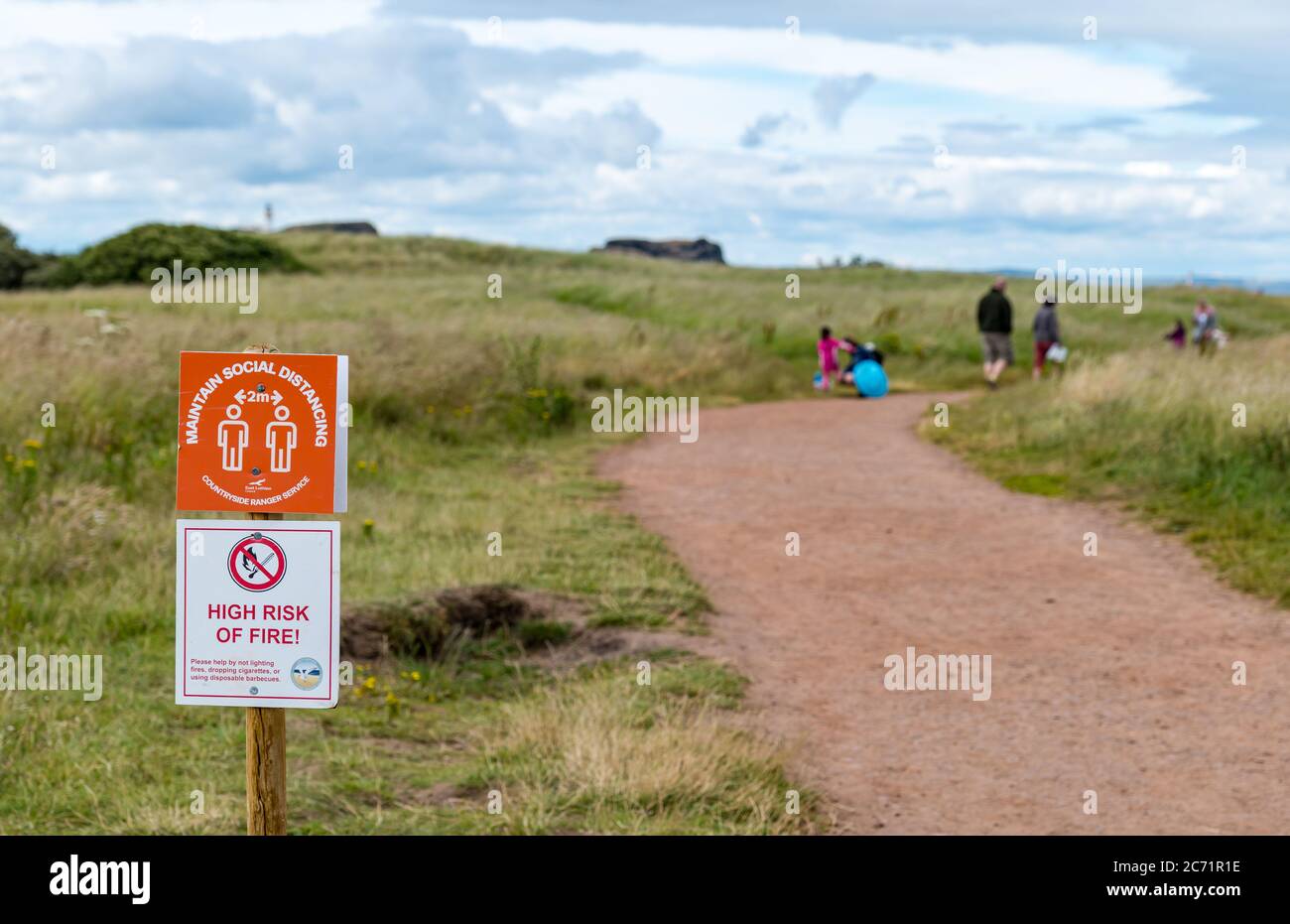East Lothian, Scotland, United Kingdom, 13th July 2020. UK Weather: overcast at Yellowcraig beach after rain. Social distancing measures are in place on the route from the carpark to the beach during the Covid-19 coronavirus pandemic as people walk along the footpath with a notice to stay 2 metres apart and a warning about the fire risk Stock Photo