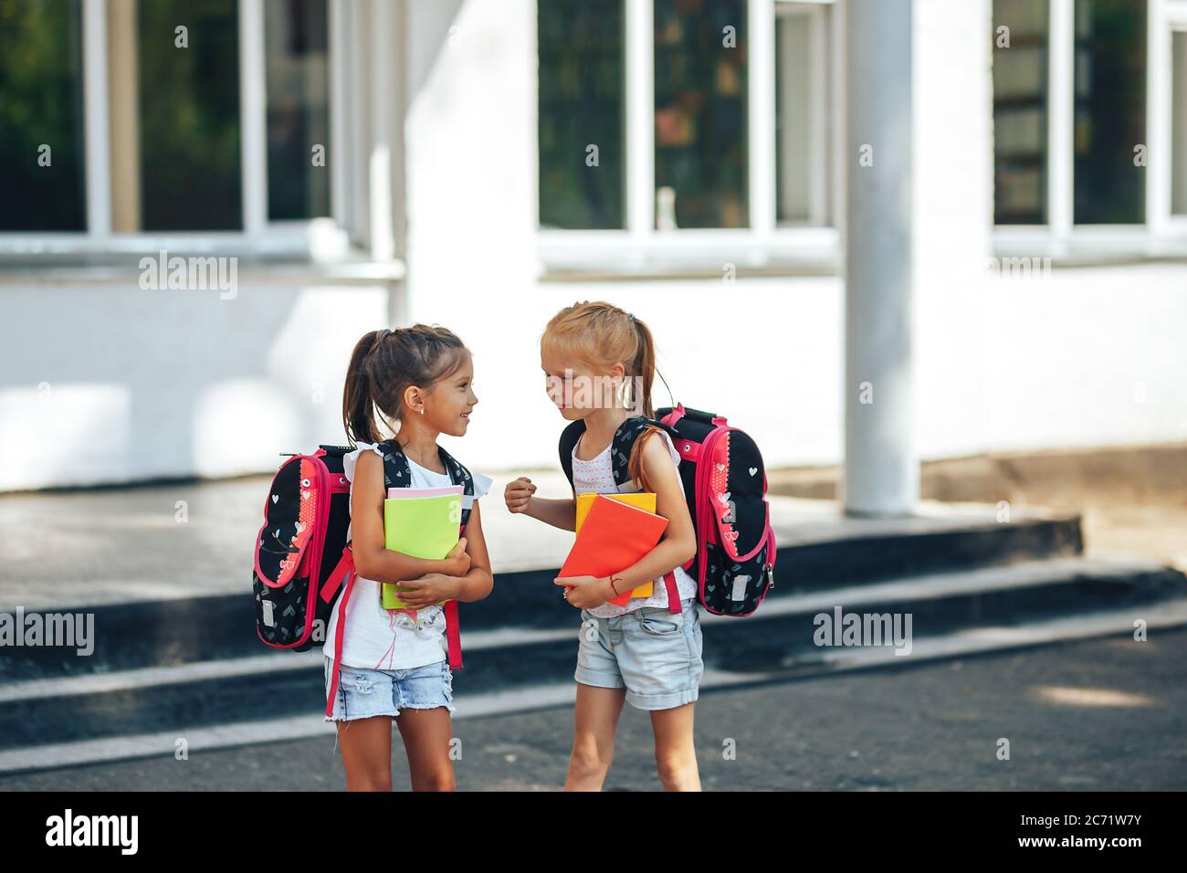 Two schoolgirls are talking near the school, back to school, primary education of children Stock Photo