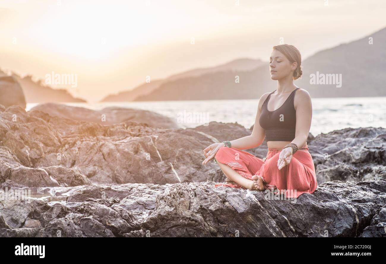 A young girl sitting in yoga meditation by the beach at sunset Stock Photo