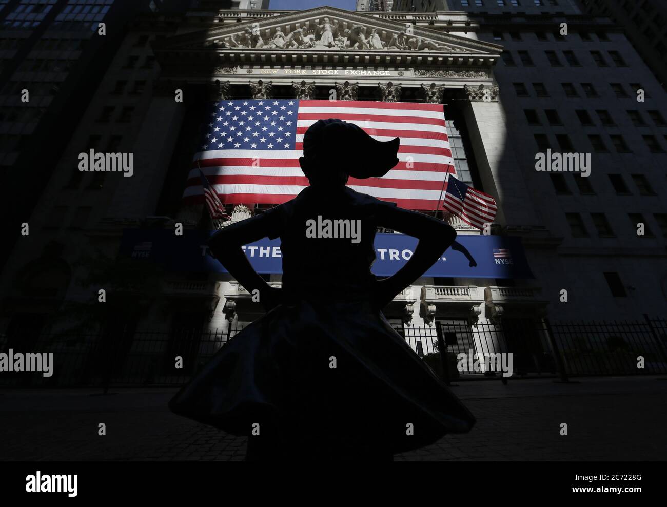 New York, United States. 13th July, 2020. The Fearless Girl Statue faces a giant American Flag that hangs outside of The New York Stock Exchange just after the opening bell on Wall Street in New York City on Monday, July 13, 2020. The Dow Jones Industrial Average was up over 400 points half way through the trading day even though there is coronavirus spike in some parts of the country. Photo by John Angelillo/UPI Credit: UPI/Alamy Live News Stock Photo