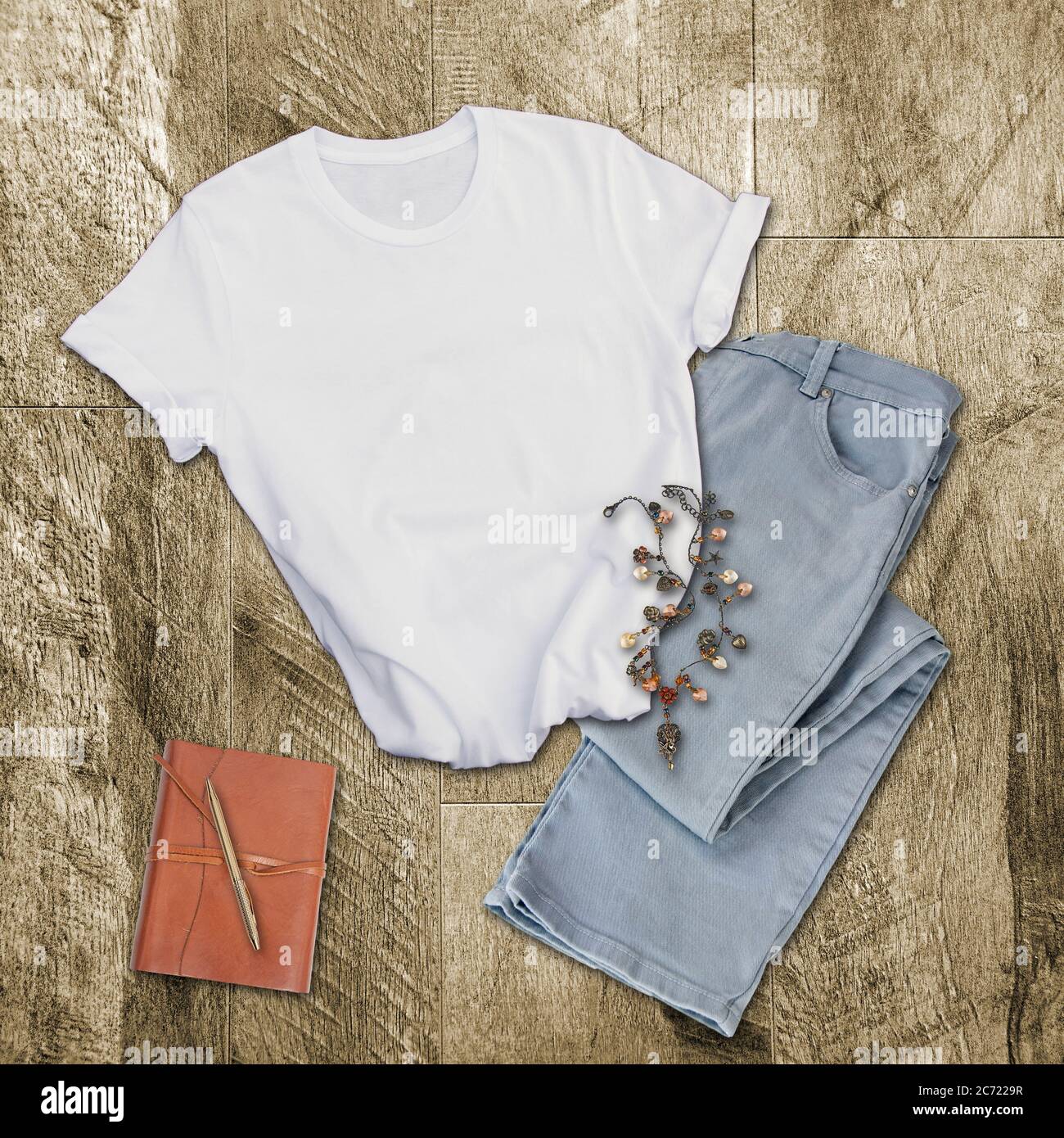 White tshirt mockup fashion clothing.   Gray pants, white shirt, leather diary and pen and a boho necklace on a wood background with room for text for Stock Photo