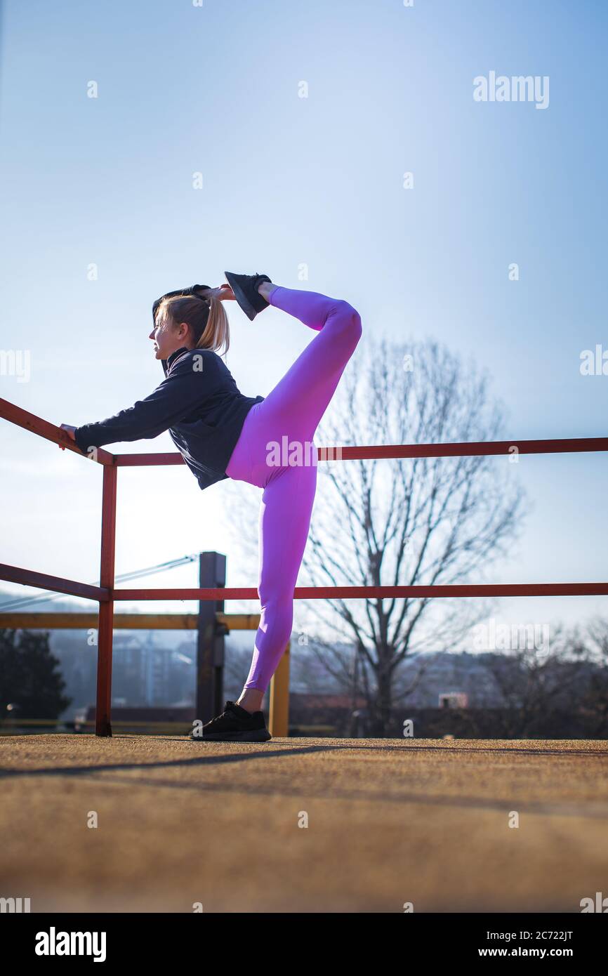 flexible young woman stretching outdoors and and lifting leg extremely high Stock Photo