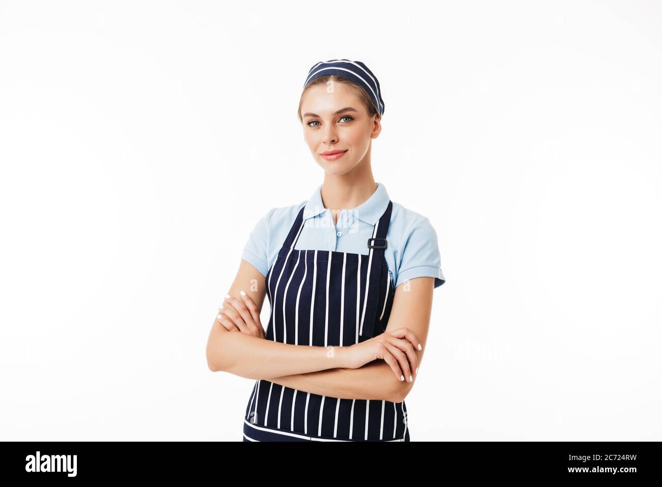 Beautiful woman cook in striped apron and cap dreamily looking in camera with arms folded over white background isolated Stock Photo