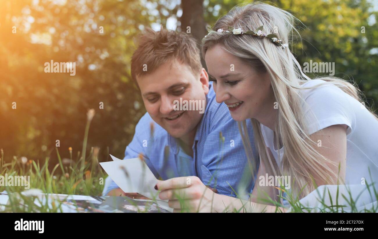 A guy and a girl are watching a family album with photos in the park on the grass. Stock Photo