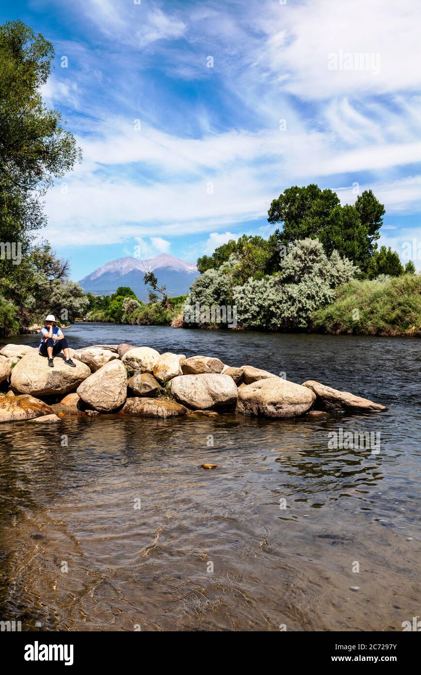 Senior woman relaxing on rocks along the Arkansas RIver which runs through the downtown historic district of the small mountain town of Salida, Colora Stock Photo