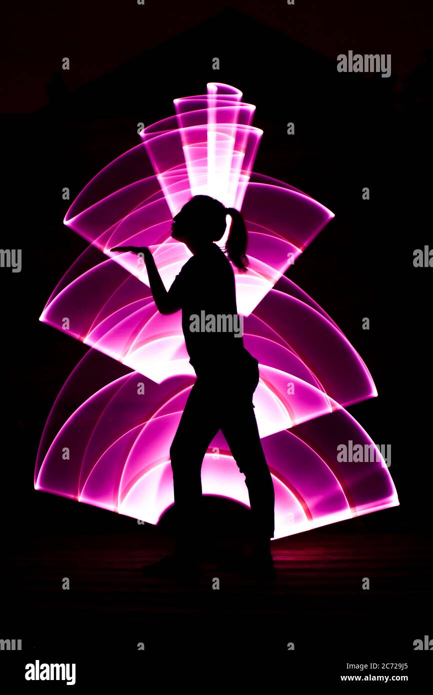 Silhouette of a woman in profile doing a kisses. Abstract curved shape, pink color with a light saber in the background. Lightpainting session. Stock Photo