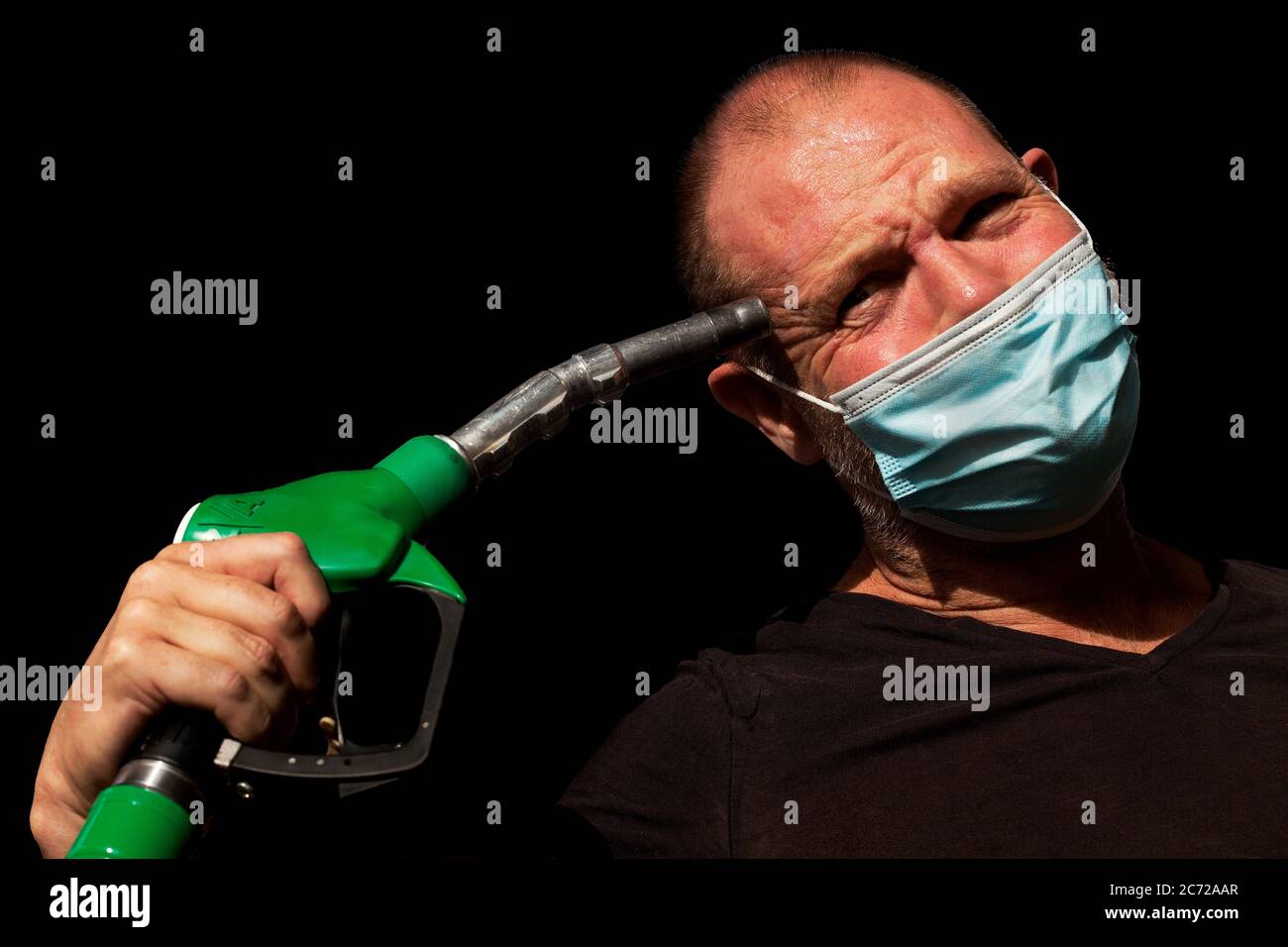 Man jokingly holds fuel nozzle to his head. Stock Photo