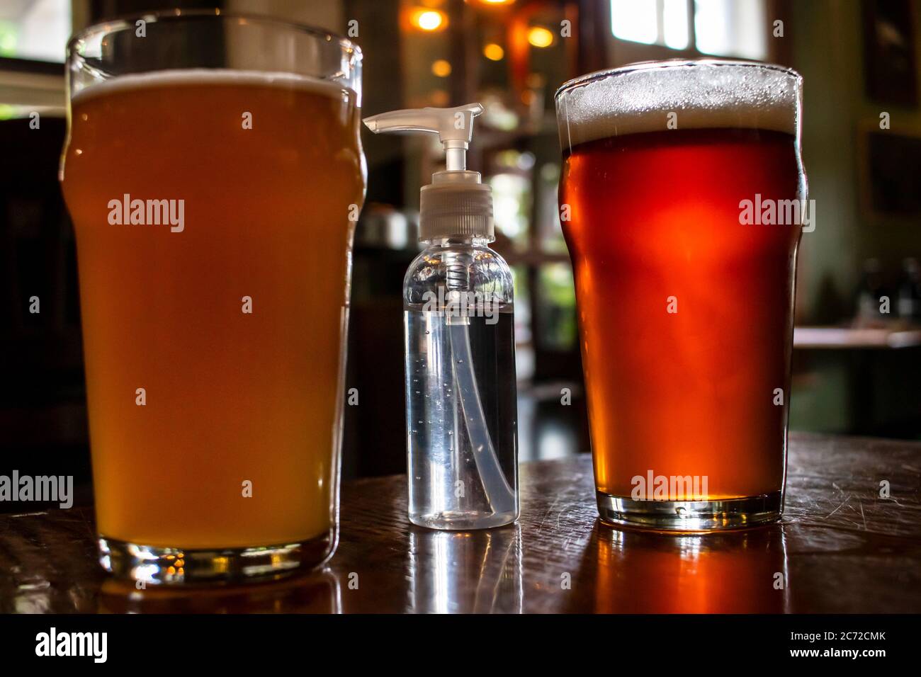 July, 2020 - Joliette, Qc, Canada: Two Pints of draft beer and Hand Sanitizer Pump Bottle in a reopened pub, COVID-19 Coronavirus Pandemic reopening Stock Photo