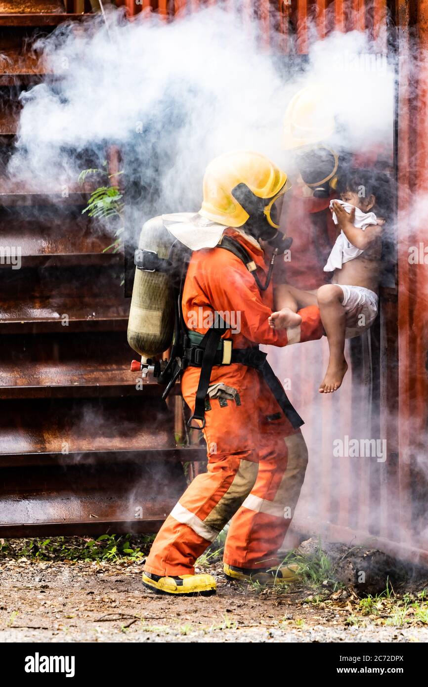 Firefighter rescue girl little child from burning building. He hold the girl and rescue her through window of building. Firefighter safety rescue from Stock Photo