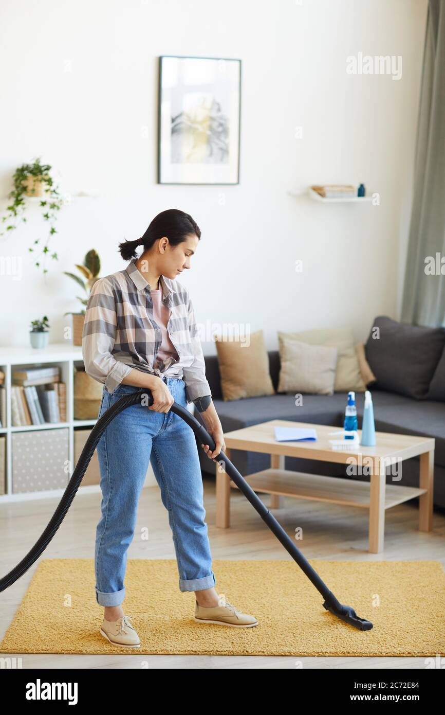 Young woman using vacuum cleaner to vacuum the carpet in the living ...