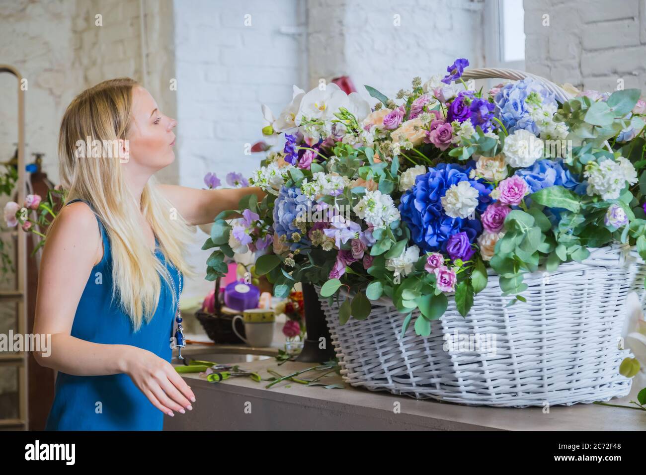 Portrait of professional woman floral artist, florist making large floral basket with flowers at workshop, flower shop. Floristry, handmade, wedding Stock Photo