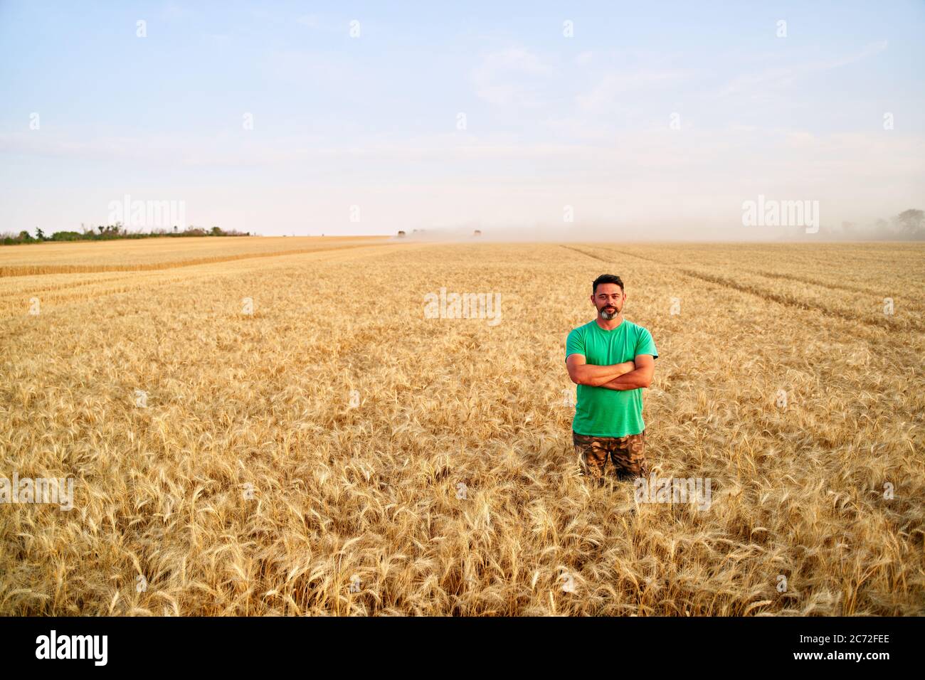 Happy farmer proudly standing in wheat field with arms crossed on chest ...