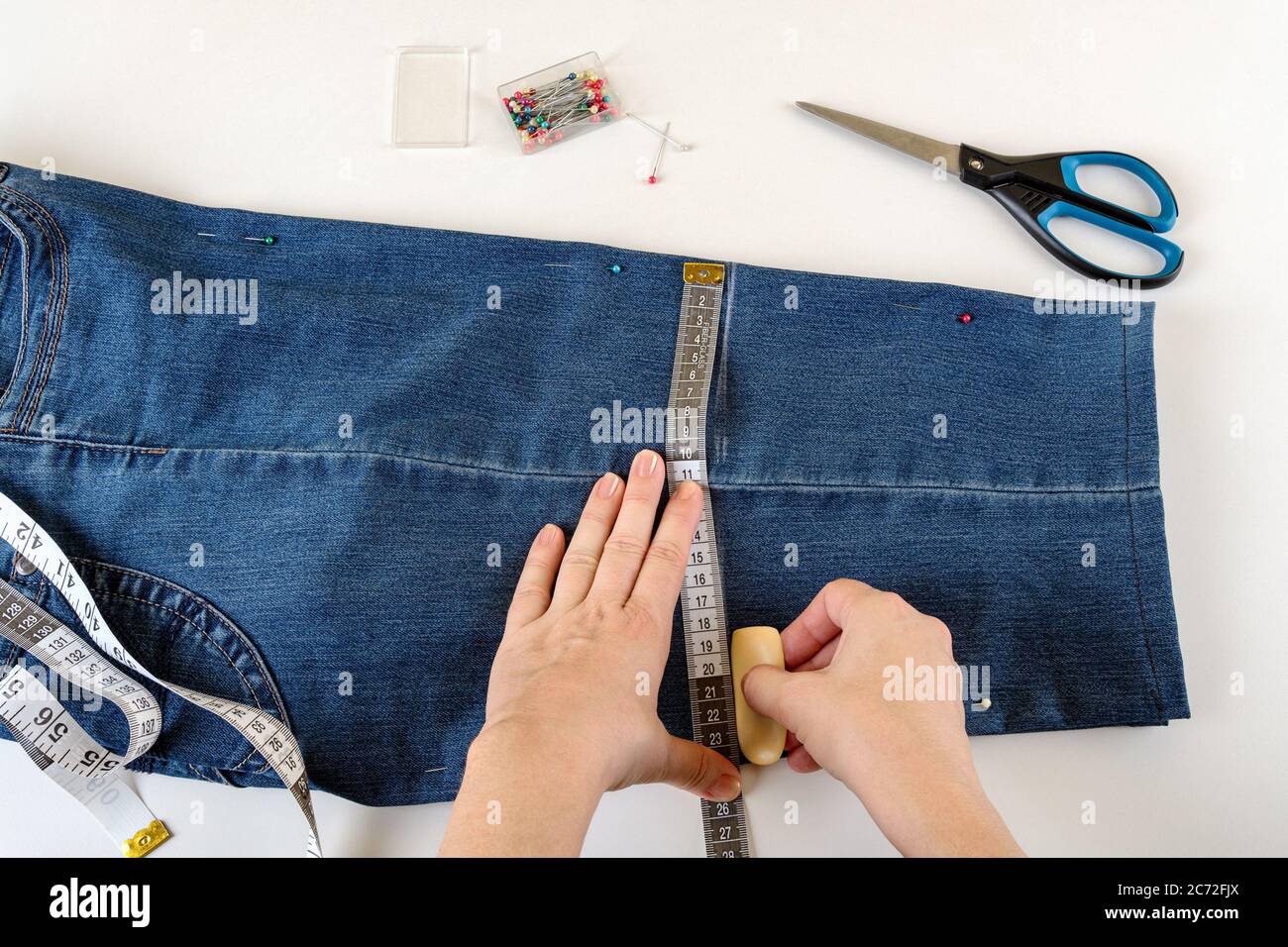 Caucasian woman hands drawing a cut line on a folded in half blue denim  capris on a white table. Shorten the jeans with scissors and sewing pin. DIY  Stock Photo - Alamy