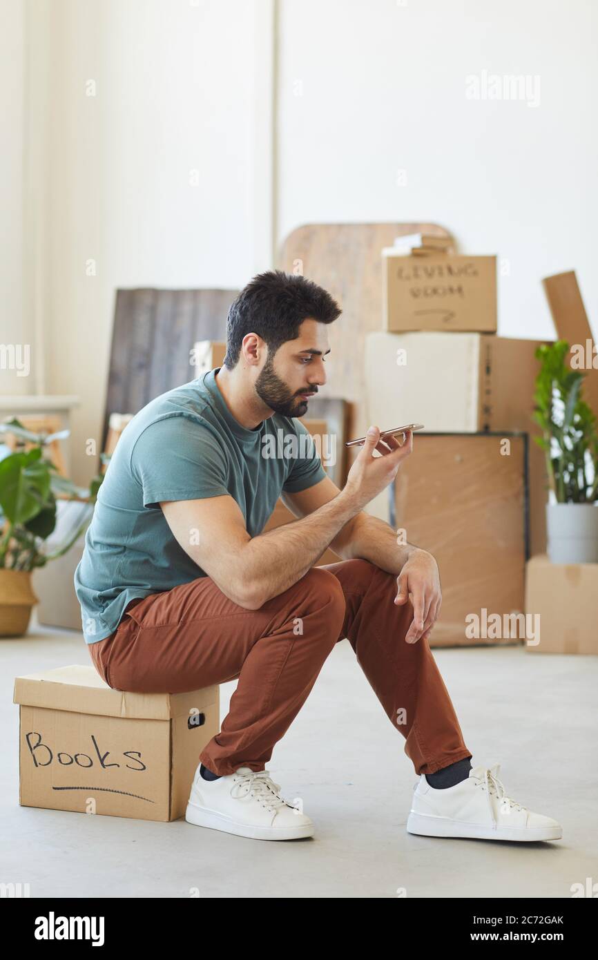 Young bearded man sitting on the box and using his mobile phone during relocation Stock Photo
