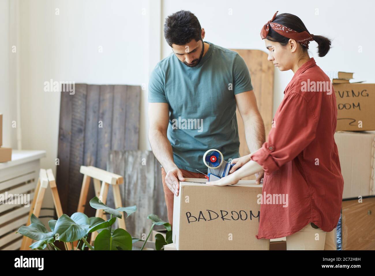 Young couple packing things in the boxes and using adhesive tape during relocation Stock Photo
