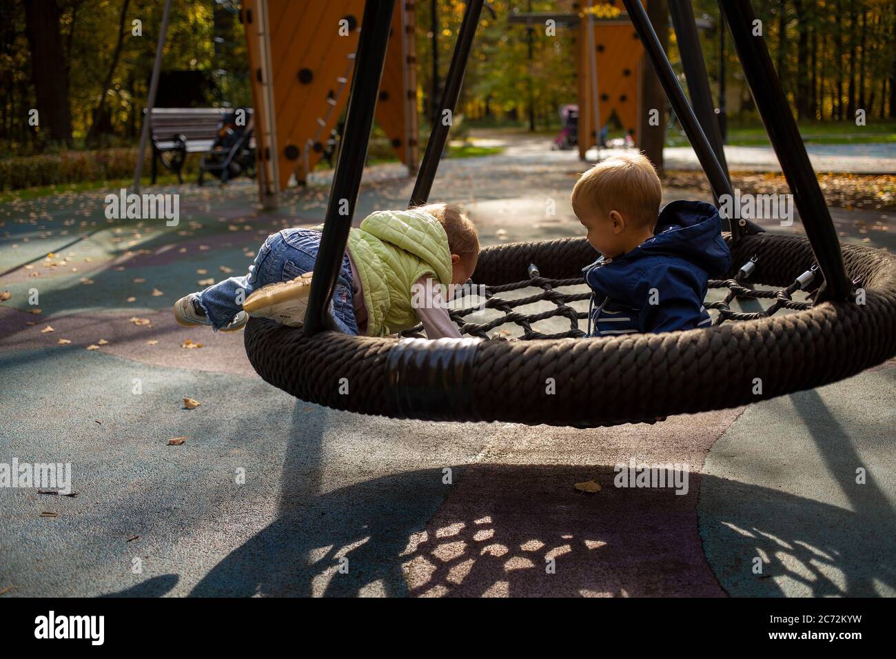 two toddlers a boy and a girl play cheerfully and swing on a swing hammock  on a playground in the autumn park Stock Photo - Alamy