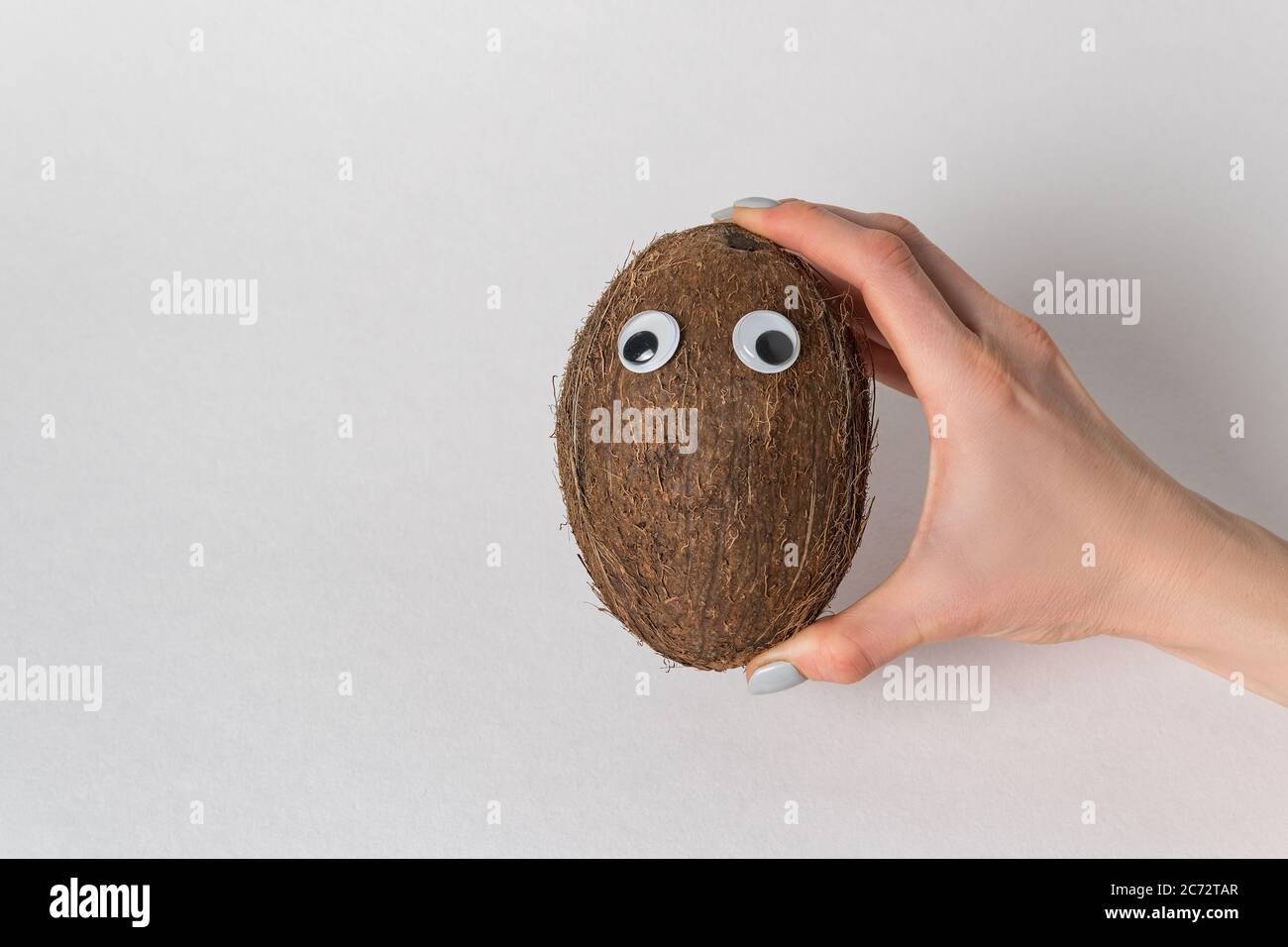 hand holds the coconut with Googly eyes on white background. coconut