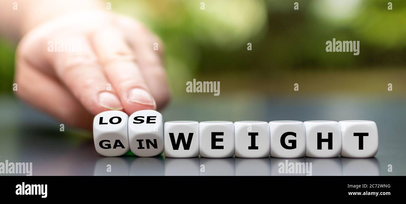 Hand turns dice and changes the expression 'gain weight' to 'lose weight'. Stock Photo