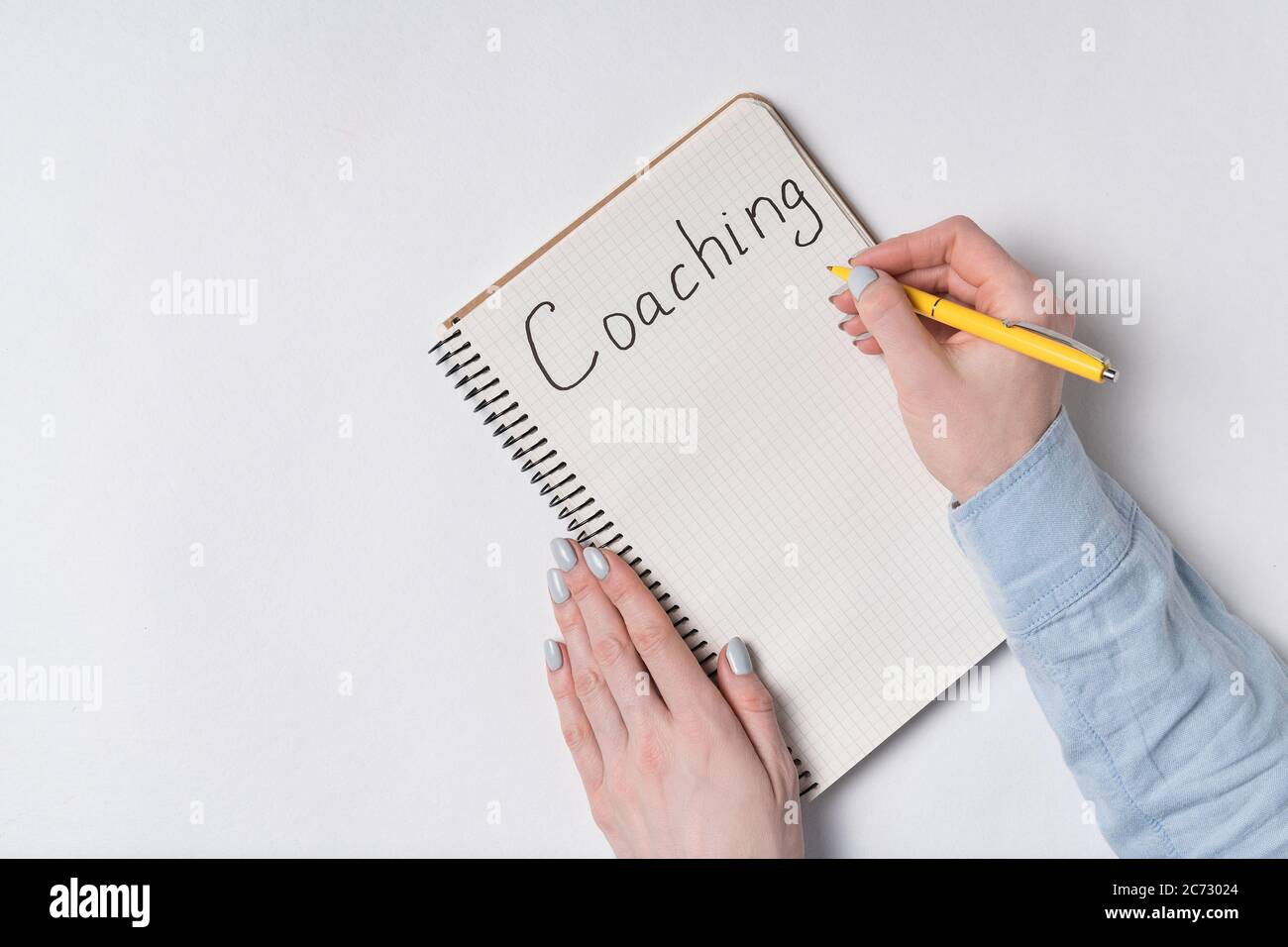 Female hands writes word COACHING in notepad. White background. Top ...