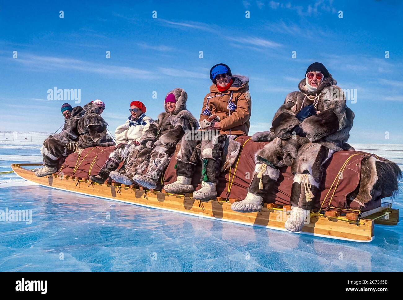 Visitors and local Inuit elders, dressed in traditional caribou skin clothing, sitting on a traditional Inuit cargo sled, also called a komatik. Stock Photo
