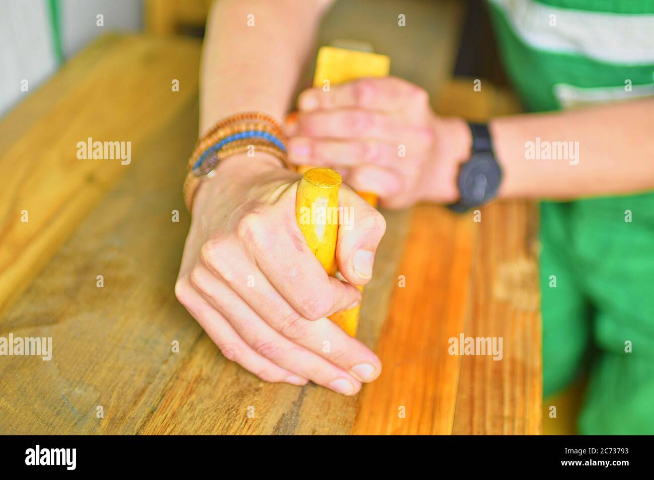 Carpenter working with plane on table in his workshop. Carpenter working with plane in a carpentry shop. Young carpenter wearing bracelets Stock Photo