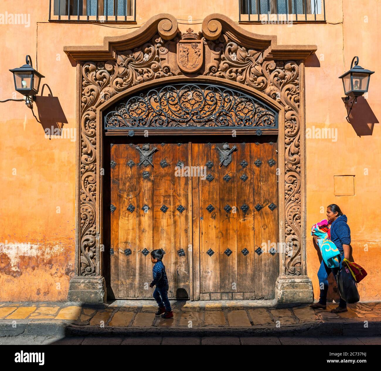 Indigenous mexican maya woman walking by a decorated door in colonial style architecture with her children, San Cristobal de las Casas, Mexico Stock Photo