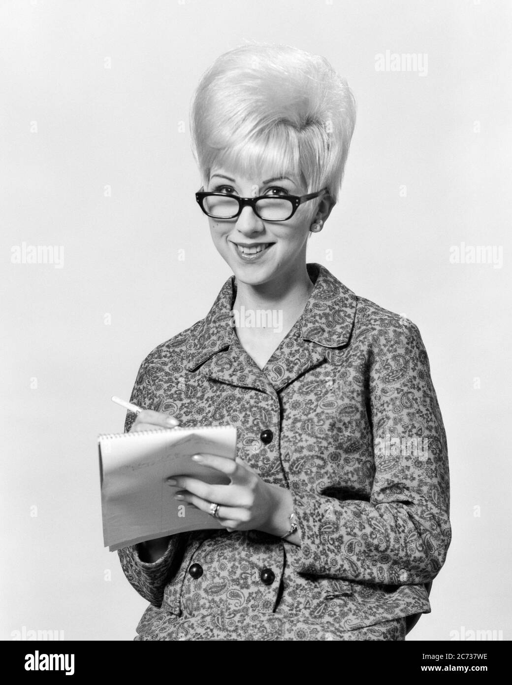 1960s SMILING BLONDE WOMAN SECRETARY IN WOOL SUIT WITH BOUFFANT HAIRDO  WEARING CAT EYE GLASSES LOOKING AT CAMERA TAKING NOTES - asp jo7378a ASP001  HARS STYLE PAD COMMUNICATION CAREER BLOND YOUNG ADULT