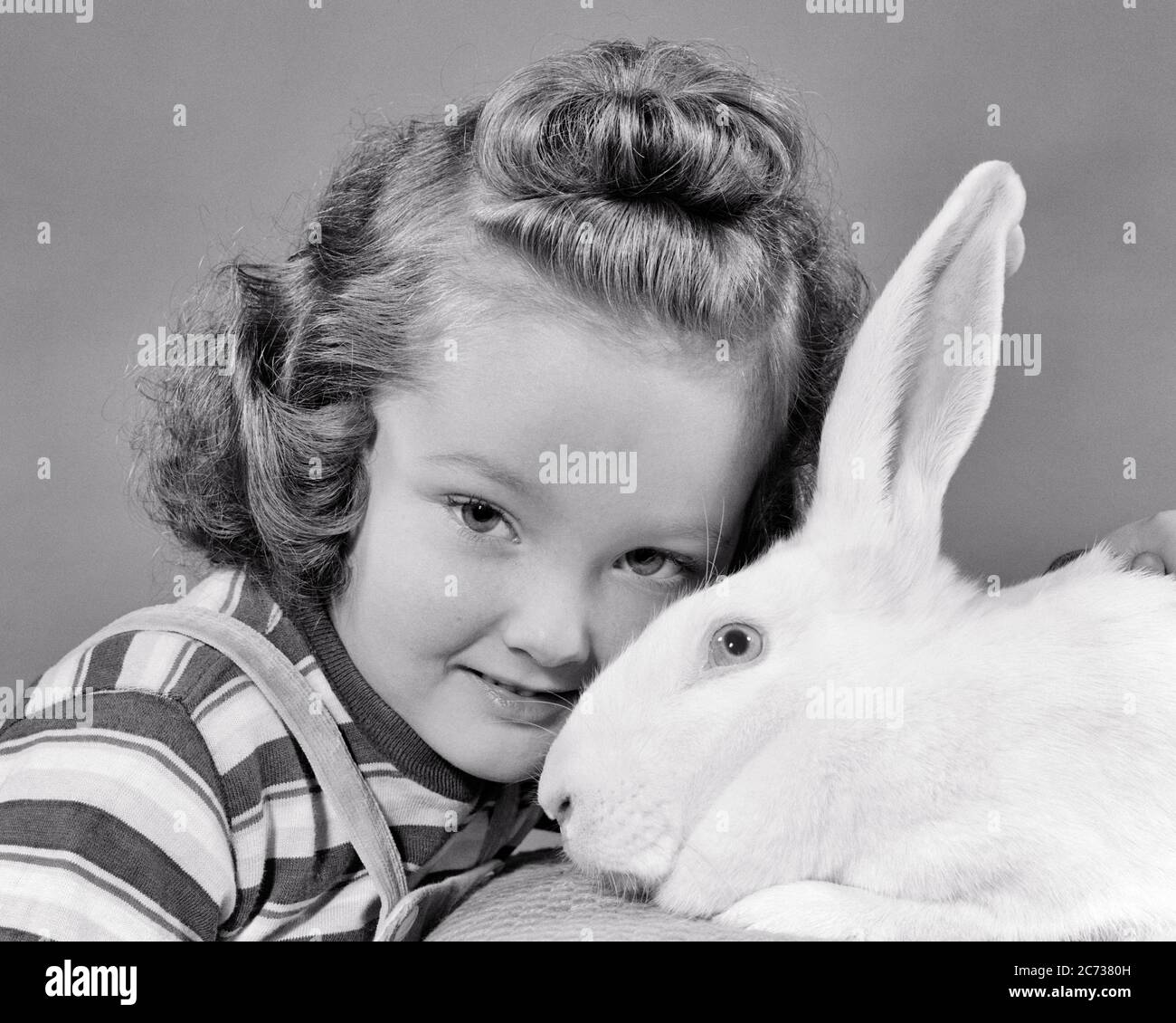 1940s LITTLE GIRL LOOKING AT CAMERA HEAD TO HEAD WITH A WHITE RABBIT - e47 HAR001 HARS B&W EYE CONTACT HAPPINESS HEAD AND SHOULDERS CHRISTIANITY RESURRECTION BUNNY EASTER BUNNY WHITE RABBIT JUVENILES TEE SHIRT BLACK AND WHITE CAUCASIAN ETHNICITY HAR001 HEAD TO HEAD OLD FASHIONED Stock Photo