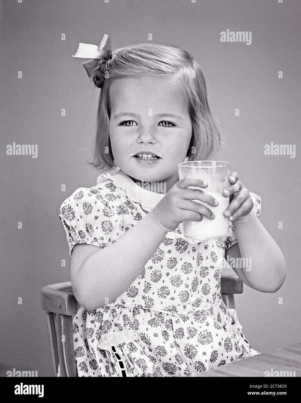 1940s LITTLE BLONDE GIRL BOW IN HER HAIR PRINT DRESS DRINKING A GLASS OF MILK SITTING AT CHILD’S TABLE AND CHAIR - f369 HAR001 HARS STUDIO SHOT HEALTHINESS HOME LIFE DAIRY COPY SPACE HALF-LENGTH B&W HAPPINESS WELLNESS BEVERAGE AND FLUID PRINT DRESS CONSUME CONSUMING HYDRATION CHILD'S GROWTH JUVENILES PROTEIN REFRESHING BEVERAGES BLACK AND WHITE CAUCASIAN ETHNICITY HAR001 OLD FASHIONED Stock Photo
