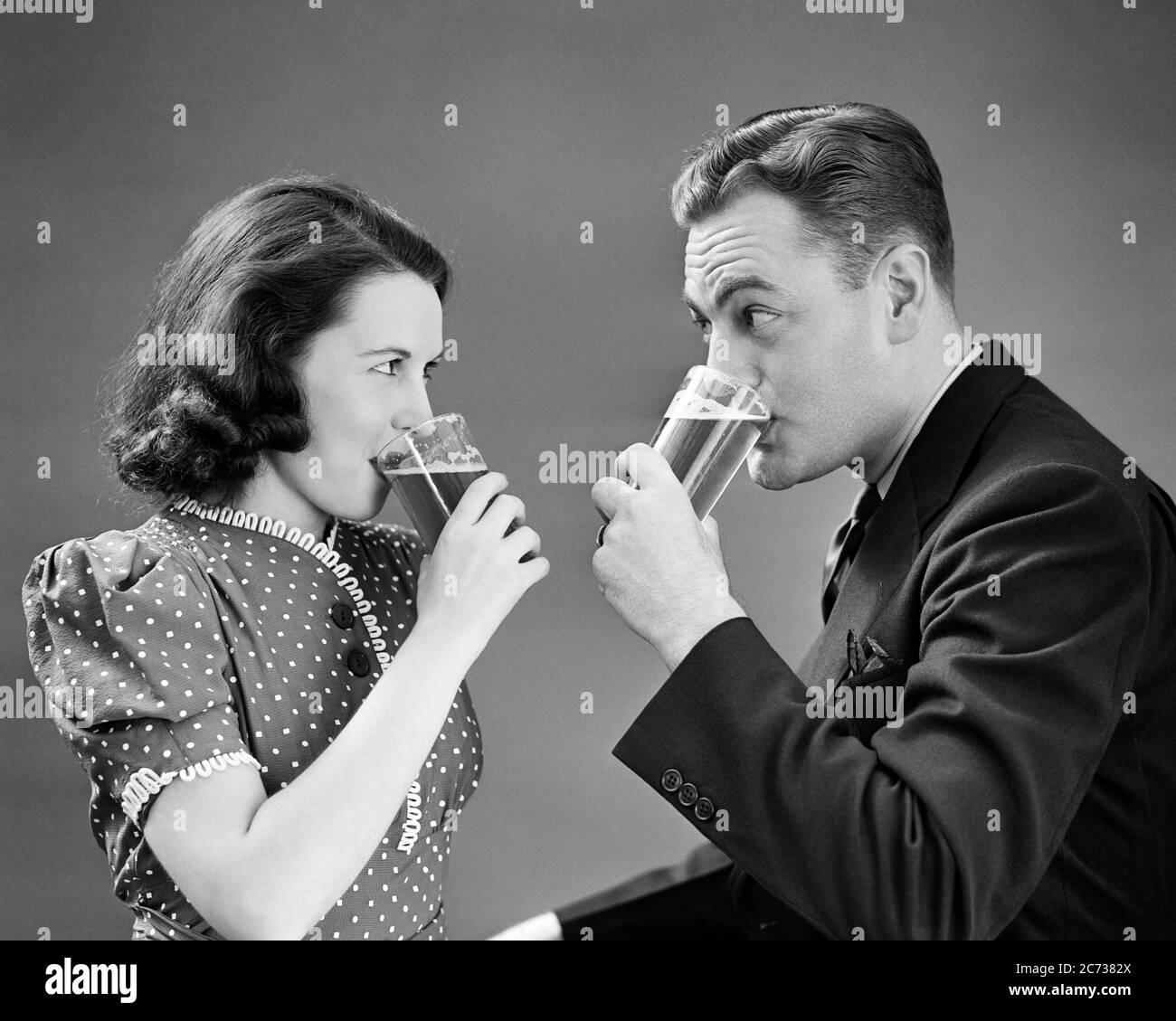 1940s COUPLE FACING ONE ANOTHER EACH DRINKING A GLASS OF BEER WOMAN WEARING POLKA DOT DRESS MAN A SUIT AND TIE - f9748 HAR001 HARS SATISFACTION FEMALES MARRIED STUDIO SHOT SPOUSE HUSBANDS HOME LIFE FACING COPY SPACE FRIENDSHIP HALF-LENGTH LADIES PERSONS MALES B&W PARTNER DATING DOT BEVERAGE POLKA AND FLUID CONNECTION ANOTHER BREWSKI TOGETHERNESS WIVES YOUNG ADULT MAN YOUNG ADULT WOMAN BEVERAGES BLACK AND WHITE CAUCASIAN ETHNICITY HAR001 OLD FASHIONED Stock Photo