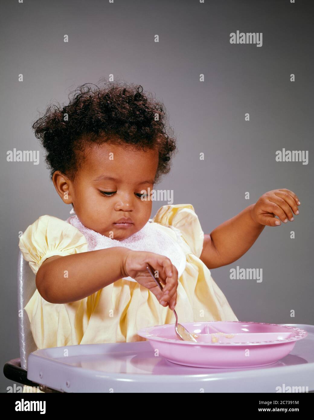 1960s INTENT AFRICAN-AMERICAN BABY GIRL SITTING IN HIGH CHAIR LEARNING TO FEED HERSELF PLAYING WITH HER FOOD WITH A SPOON  - kn398 HAR001 HARS COPY SPACE HALF-LENGTH INSPIRATION FEED CONFIDENCE SUCCESS DISCOVERY AFRICAN-AMERICANS AFRICAN-AMERICAN PROGRESS BLACK ETHNICITY A IN OPPORTUNITY TO CONNECTION CONCEPTUAL STYLISH MOTIVATED FOCUSED GROWTH HERSELF JUVENILES BABY GIRL HAR001 INTENT OLD FASHIONED AFRICAN AMERICANS Stock Photo