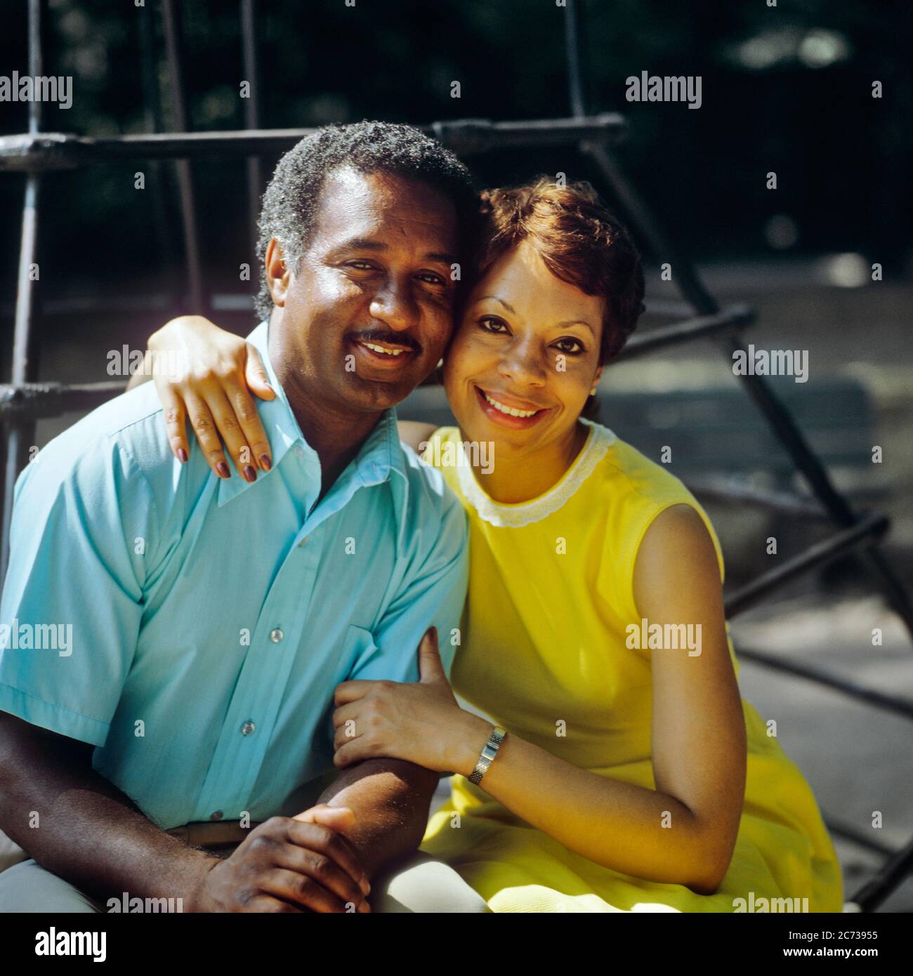 1980s PORTRAIT SMILING AFRICAN AMERICAN COUPLE SITTING SIDE BY SIDE HUGGING LOOKING AT CAMERA MAN BLUE SHIRT WOMAN YELLOW DRESS  - kp3826 TEU001 HARS OLD TIME NOSTALGIA HUGGING OLD FASHION 1 FACIAL STYLE EMBRACE TOUCH PLEASED JOY LIFESTYLE FEMALES MARRIED SPOUSE HUSBANDS HEALTHINESS HOME LIFE COPY SPACE FRIENDSHIP HALF-LENGTH HUG LADIES PERSONS MALES EMBRACING EXPRESSIONS PARTNER EYE CONTACT HAPPINESS CHEERFUL AFRICAN-AMERICANS AFRICAN-AMERICAN BLACK ETHNICITY PRIDE SMILES CONNECTION CONCEPTUAL JOYFUL STYLISH MID-ADULT MID-ADULT MAN MID-ADULT WOMAN SIDE BY SIDE TOGETHERNESS WIVES OLD FASHIONED Stock Photo