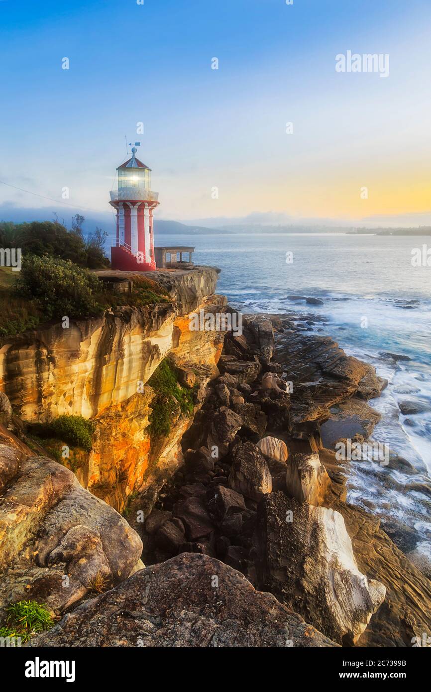 Hornby lighthouse at the edge of sandstone cliff eroded by Pacific ocean tides and waves shining at sunrise. Stock Photo