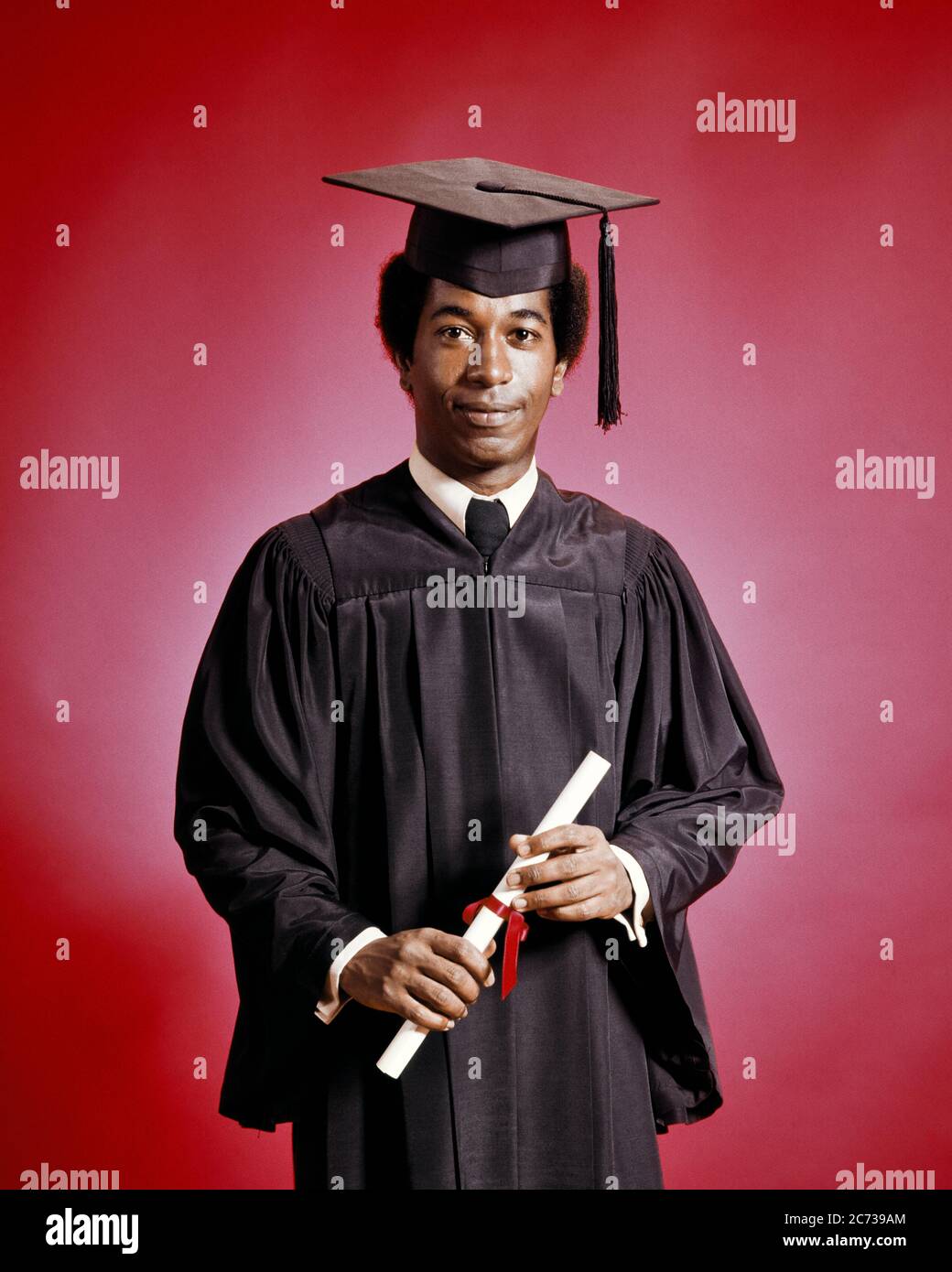 1970s SERIOUS PROUD AFRICAN-AMERICAN MAN GRADUATE HOLDING DIPLOMA WEARING  GRADUATION ROBE MORTARBOARD SMILING LOOKING AT CAMERA - ks13064 HAR001 HARS  ROBE COPY SPACE HALF-LENGTH PERSONS INSPIRATION MALES GRADUATING CONFIDENCE  EXPRESSIONS EYE CONTACT