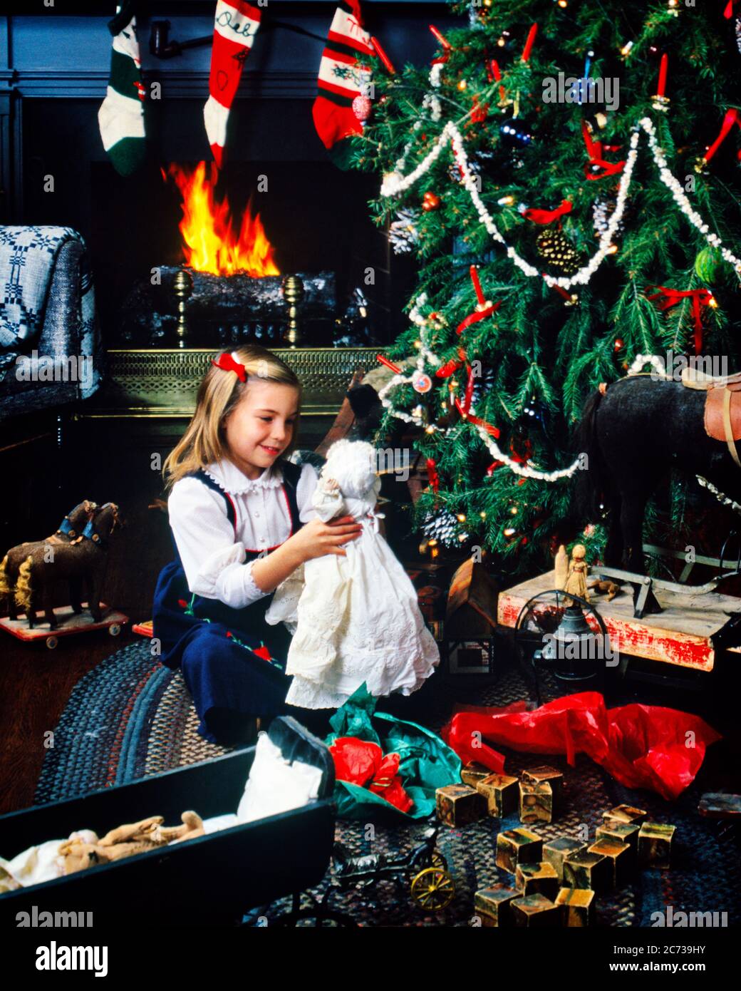 1970s 1980s SMILING BLOND GIRL HOLDING ANTIQUE DOLL SITTING BY TRADITIONAL CHRISTMAS TREE AND FIREPLACE ANTIQUE TOYS ALL AROUND - kx8796 PHT001 HARS CELEBRATION FEMALES HEAT HOME LIFE COPY SPACE HALF-LENGTH INSPIRATION TRADITIONAL CARING AMERICANA DREAMS HAPPINESS DISCOVERY MERRY PORCELAIN EXCITEMENT MODELS DECEMBER CONCEPTUAL DECEMBER 25 WARMTH IMAGINATION STYLISH CHRISTMAS TREE COLLECTIBLES JOYOUS JUVENILES CAUCASIAN ETHNICITY COLLECTIBLE OLD FASHIONED Stock Photo