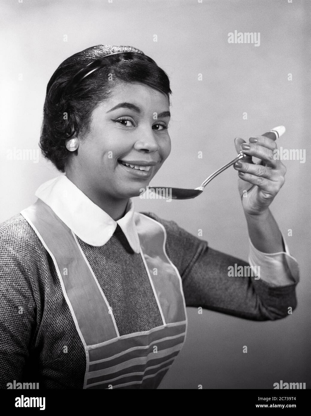 1950s 1960s AFRICAN AMERICAN WOMAN HOLDING SPOON TASTING WEARING APRON HOUSEWIFE COOKING LOOKING AT CAMERA - n153 HAR001 HARS B&W EYE CONTACT GOALS SUCCESS HOMEMAKER HAPPINESS HOMEMAKERS AFRICAN-AMERICANS AFRICAN-AMERICAN BLACK ETHNICITY PRIDE TASTE TASTING HOUSEWIVES SAMPLING STYLISH MID-ADULT MID-ADULT WOMAN SAMPLE BLACK AND WHITE FOOD PREPARATION HAR001 OLD FASHIONED AFRICAN AMERICANS Stock Photo
