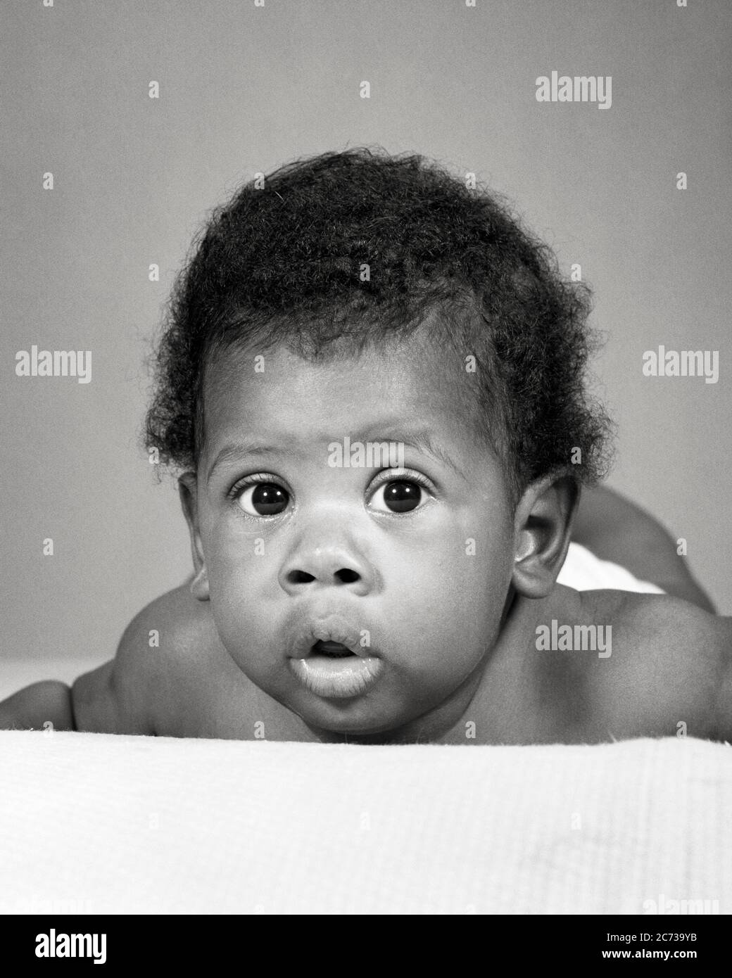 1960s AFRICAN-AMERICAN BABY LAYING ON STOMACH FUNNY FACIAL EXPRESSION - n2307 HAR001 HARS AFRICAN-AMERICANS AFRICAN-AMERICAN BLACK ETHNICITY COMICAL COMEDY BABY BOY WIDE-EYED GROWTH JUVENILES BIG EYES BLACK AND WHITE HAR001 MOUTH OPEN OLD FASHIONED AFRICAN AMERICANS Stock Photo