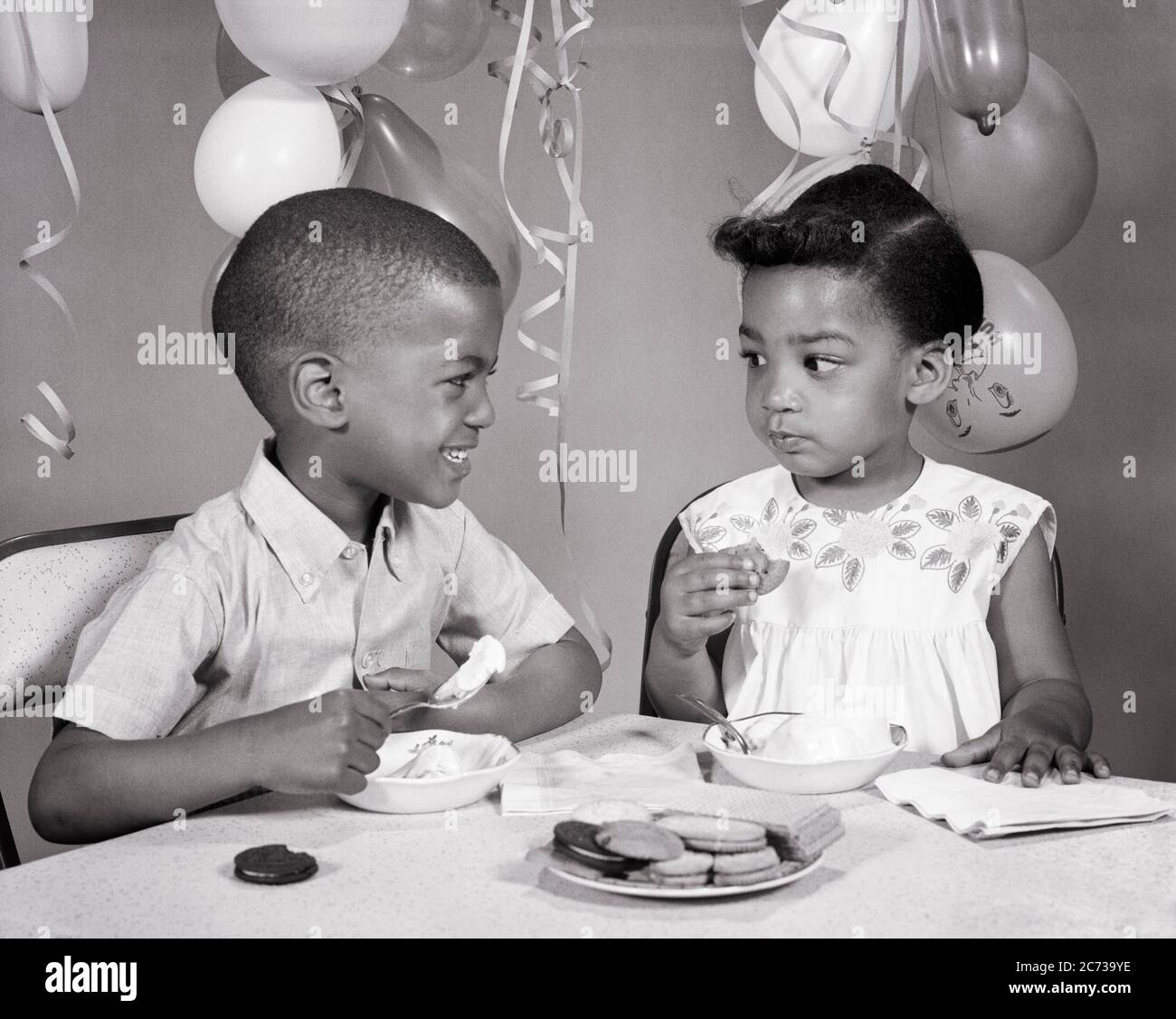 1960s TWO AFRICAN AMERICAN CHILDREN BOY GIRL BROTHER SISTER LOOKING AT EACH OTHER EATING ICE CREAM COOKIES BIRTHDAY PARTY - n2081 HAR001 HARS FACIAL COMMUNICATION COMIC PLEASED JOY LIFESTYLE FEMALES BROTHERS HOME LIFE COPY SPACE FRIENDSHIP HALF-LENGTH MALES COOKIES SIBLINGS SISTERS EXPRESSIONS B&W FROWNING HUMOROUS CHEERFUL AFRICAN-AMERICANS AFRICAN-AMERICAN ENJOYING COMICAL AT SIBLING SMILES COMEDY JOYFUL ICE CREAM GROWTH JUVENILES TOGETHERNESS BLACK AND WHITE EACH OTHER HAR001 OLD FASHIONED AFRICAN AMERICANS Stock Photo