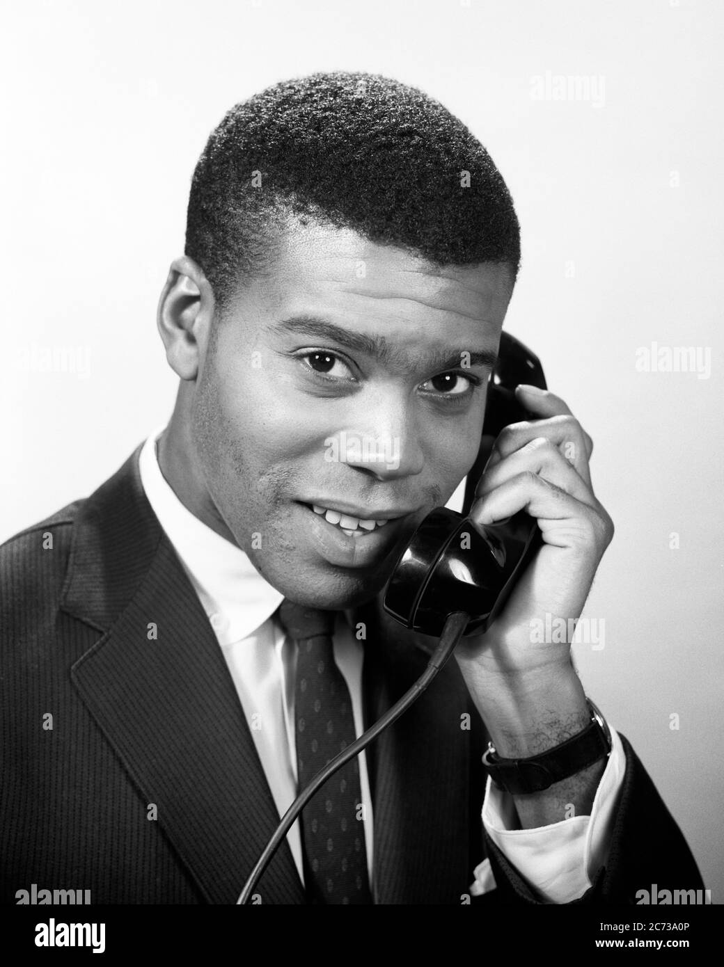 1950s 1960s SERIOUS SMILING AFRICAN AMERICAN MAN BUSINESSMAN WEARING SUIT AND TIE LOOKING AT CAMERA TALKING ON TELEPHONE  - n248 HAR001 HARS JOY LIFESTYLE HEALTHINESS HALF-LENGTH PERSONS MALES CONFIDENCE EXPRESSIONS B&W EYE CONTACT GOALS SUCCESS SUIT AND TIE DREAMS SELLING HAPPINESS HEAD AND SHOULDERS CHEERFUL CUSTOMER SERVICE AFRICAN-AMERICANS COURAGE AFRICAN-AMERICAN AND CHOICE KNOWLEDGE LEADERSHIP PROGRESS RECREATION BLACK ETHNICITY PRIDE IN ON OCCUPATIONS POLITICS SMILES CONNECTION CONCEPTUAL JOYFUL STYLISH COOPERATION GROWTH SALESMEN WEARING  YOUNG ADULT MAN BLACK AND WHITE HAR001 Stock Photo