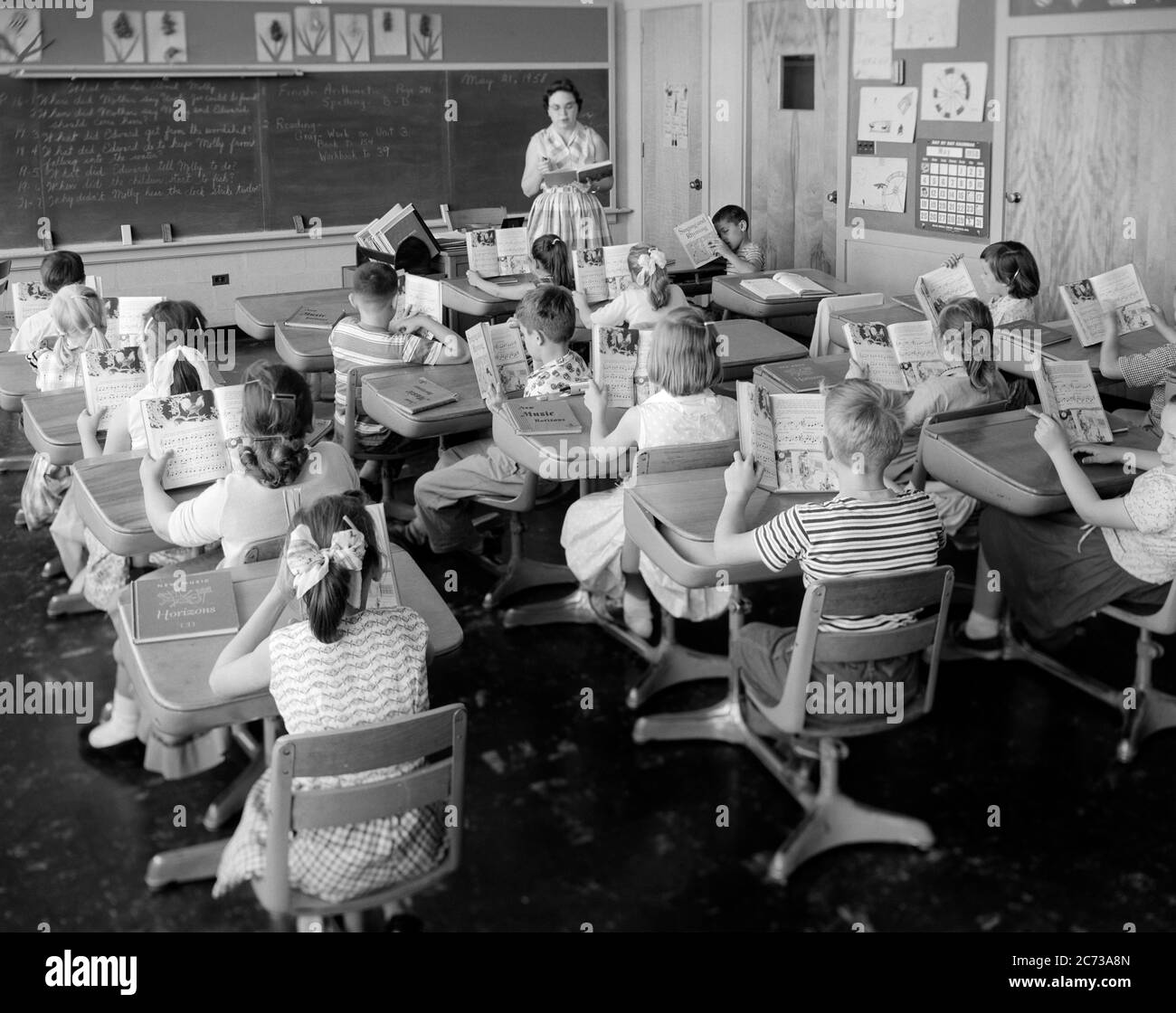 1950s 1960s ELEMENTARY SCHOOL CLASSROOM TEACHER WOMAN AND STUDENTS READING FROM OPEN TEXTBOOKS LEARNING BLACKBOARD DESKS - s12003 HEL001 HARS COPY SPACE HALF-LENGTH LADIES PERSONS INSPIRATION MALES MIDDLE-AGED B&W DESKS SCHOOLS GRADE HIGH ANGLE DISCOVERY AND INSTRUCTOR OCCUPATIONS PRIMARY TEXTBOOKS EDUCATOR COMMUNICATE COOPERATION EDUCATING EDUCATORS GRADE SCHOOL GROWTH INSTRUCTORS JUVENILES MID-ADULT WOMAN PRE-TEEN PRE-TEEN BOY PRE-TEEN GIRL SCHOOL TEACHES TOGETHERNESS BLACK AND WHITE CAUCASIAN ETHNICITY OLD FASHIONED Stock Photo