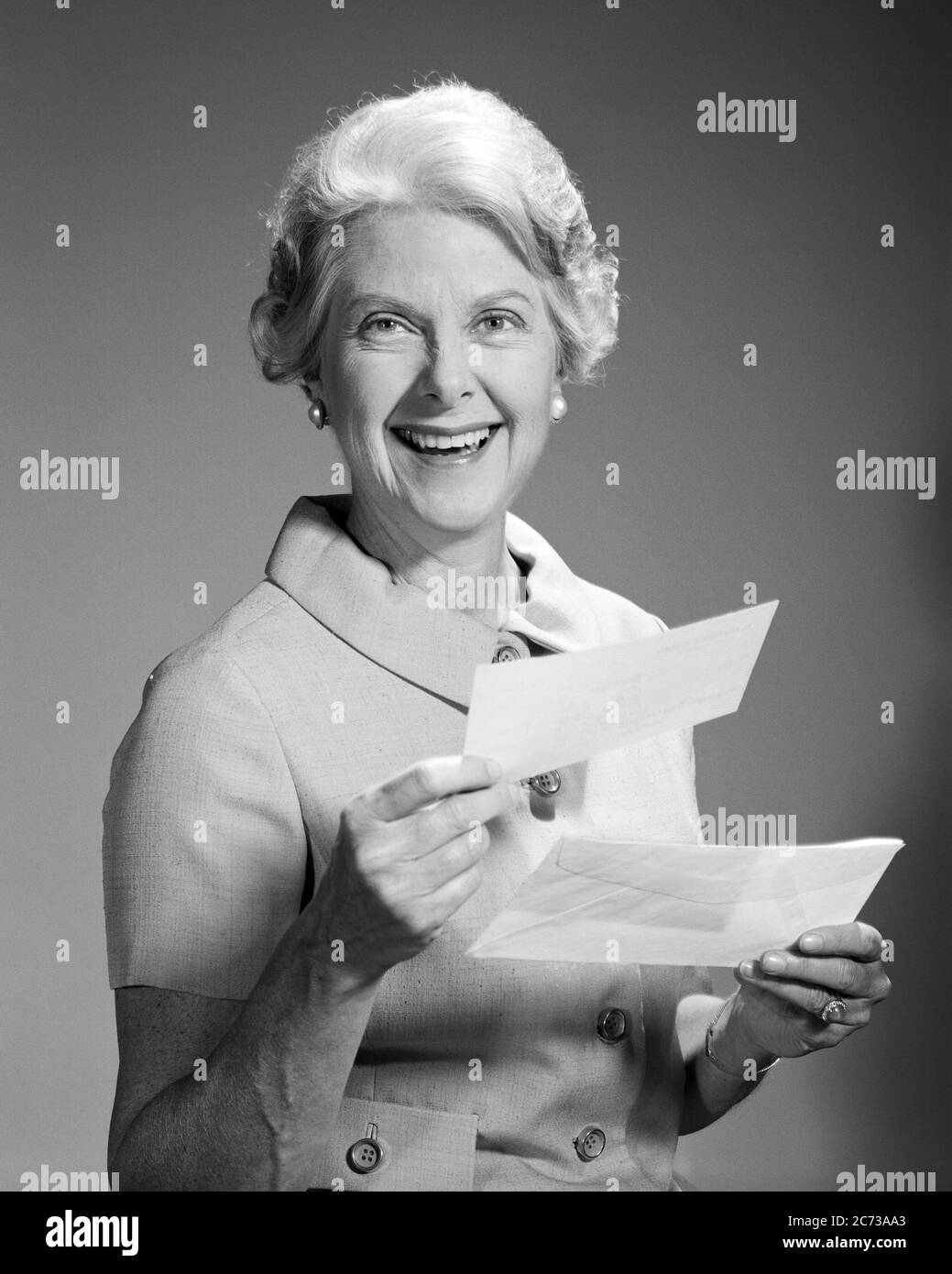 1960s SMILING SENIOR WOMAN LOOKING AT CAMERA HOLDING PAYMENT CHECK AND ENVELOPE RECEIVED IN THE MAIL - s16899 HAR001 HARS ELDER FEMALES STUDIO SHOT HOME LIFE COPY SPACE HALF-LENGTH LADIES PERSONS RETIREMENT SENIOR ADULT EXPRESSIONS B&W EYE CONTACT SENIOR WOMAN FREEDOM SUCCESS RETIREE HAPPINESS OLD AGE OLDSTERS CHEERFUL OLDSTER PROTECTION STRATEGY AND EXCITEMENT IN THE PAYMENT SMILES ELDERS CONCEPTUAL JOYFUL STYLISH RECEIVED SOCIAL SECURITY BLACK AND WHITE CAUCASIAN ETHNICITY HAR001 OLD FASHIONED Stock Photo